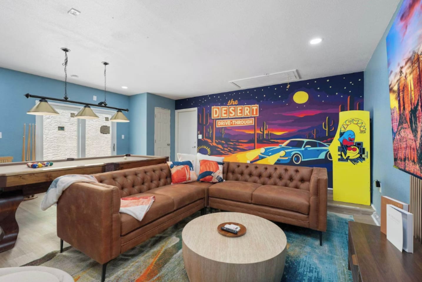 Playroom with vintage desert mural, leather seating, pool table, and arcade games—a fun, colorful space for all ages.
