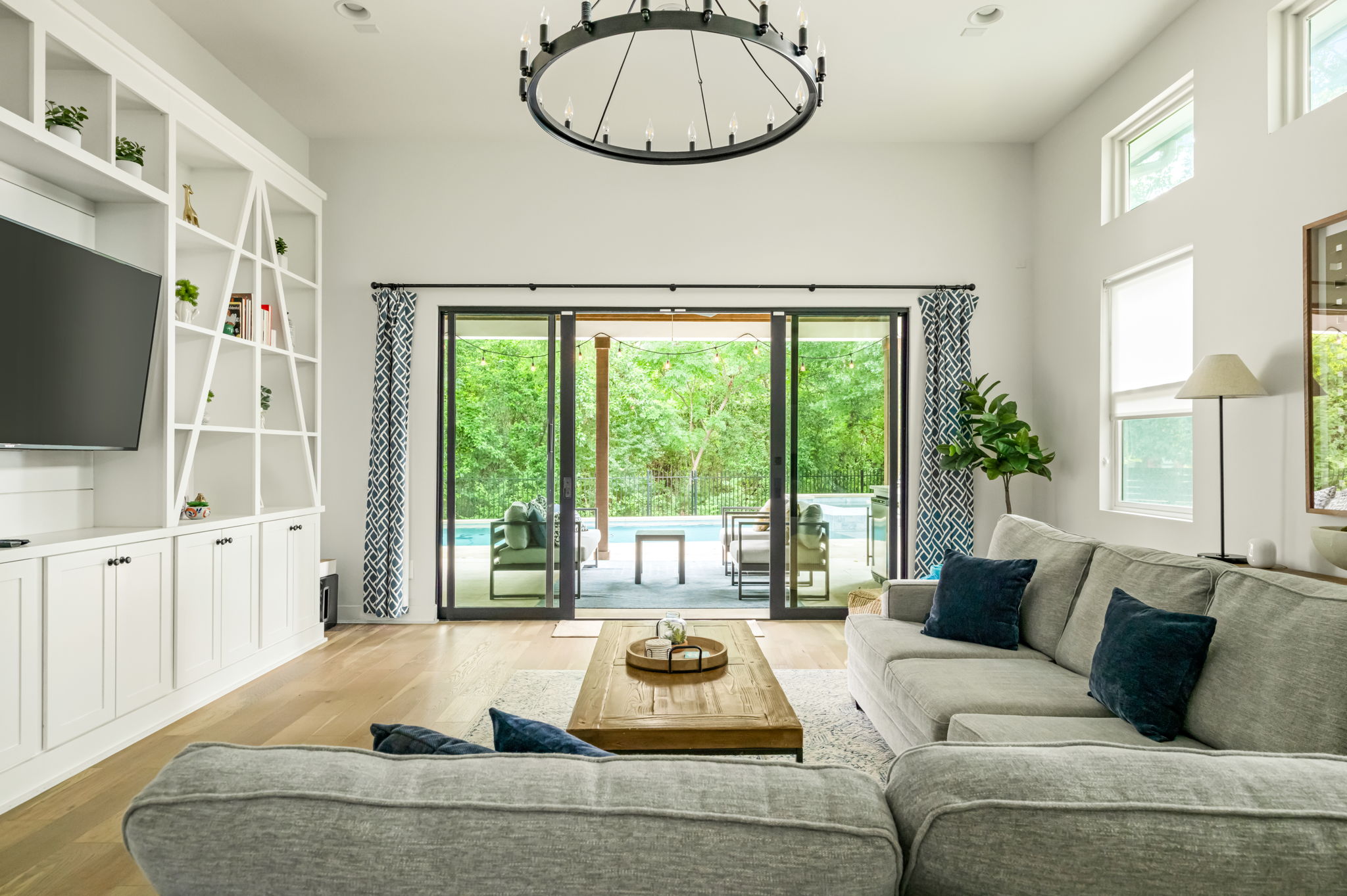 Inviting living room with a spacious sectional sofa, statement chandelier, and panoramic views of the lush backyard through wall-to-wall glass doors.
