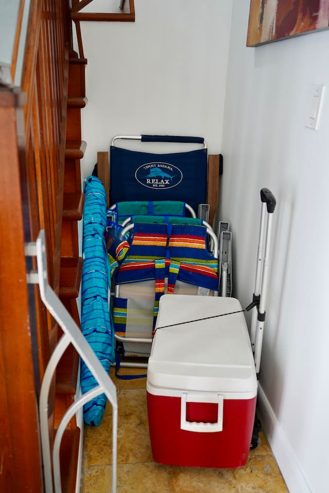 Beach gear ready to go: folding chairs, umbrella, rolling cooler, beach towels, and various beach toys