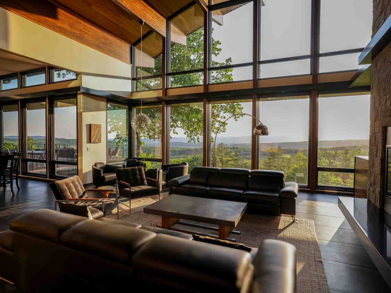 Great room with multiple seating zones, floor-to-ceiling windows, and deck beyond &mdash; Sunset Falls Berkshires estate