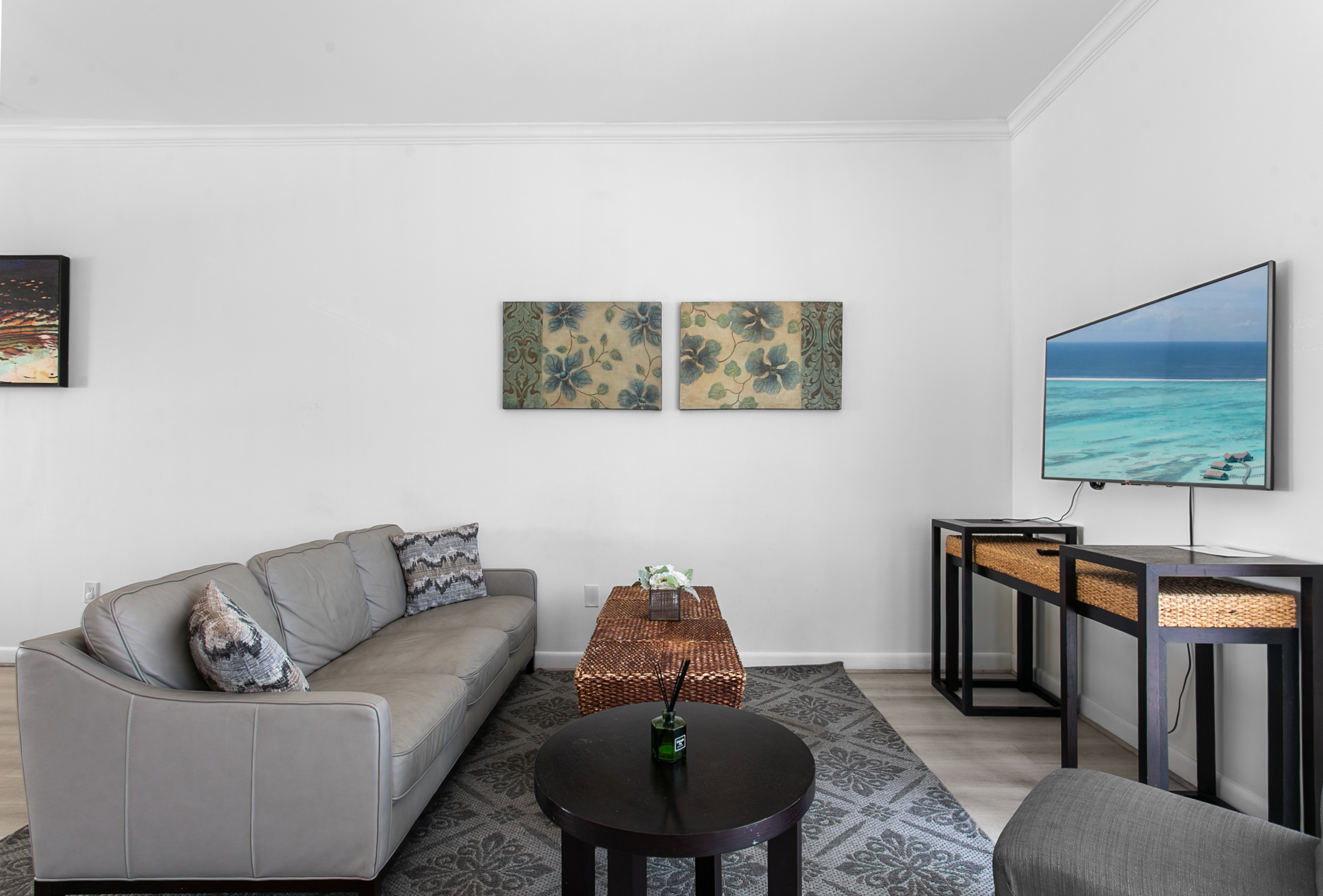 Living room with leather sofa, accent chairs, and a 50-inch flat screen TV. Sliding glass doors open to a Juliet balcony for sea breeze.