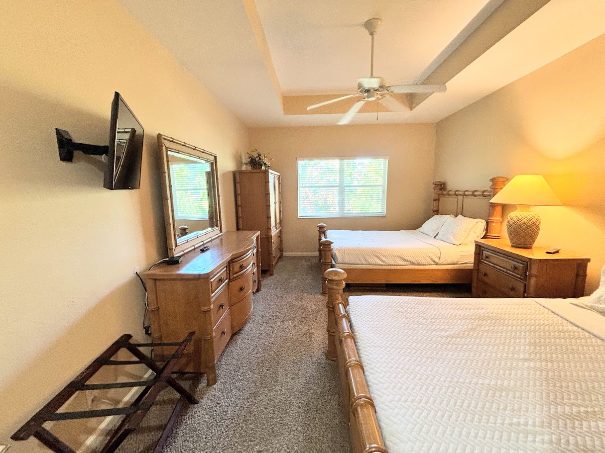 Spacious bedroom featuring two comfortable beds, tray ceiling with ceiling fan, cozy seating area, and plenty of natural light.