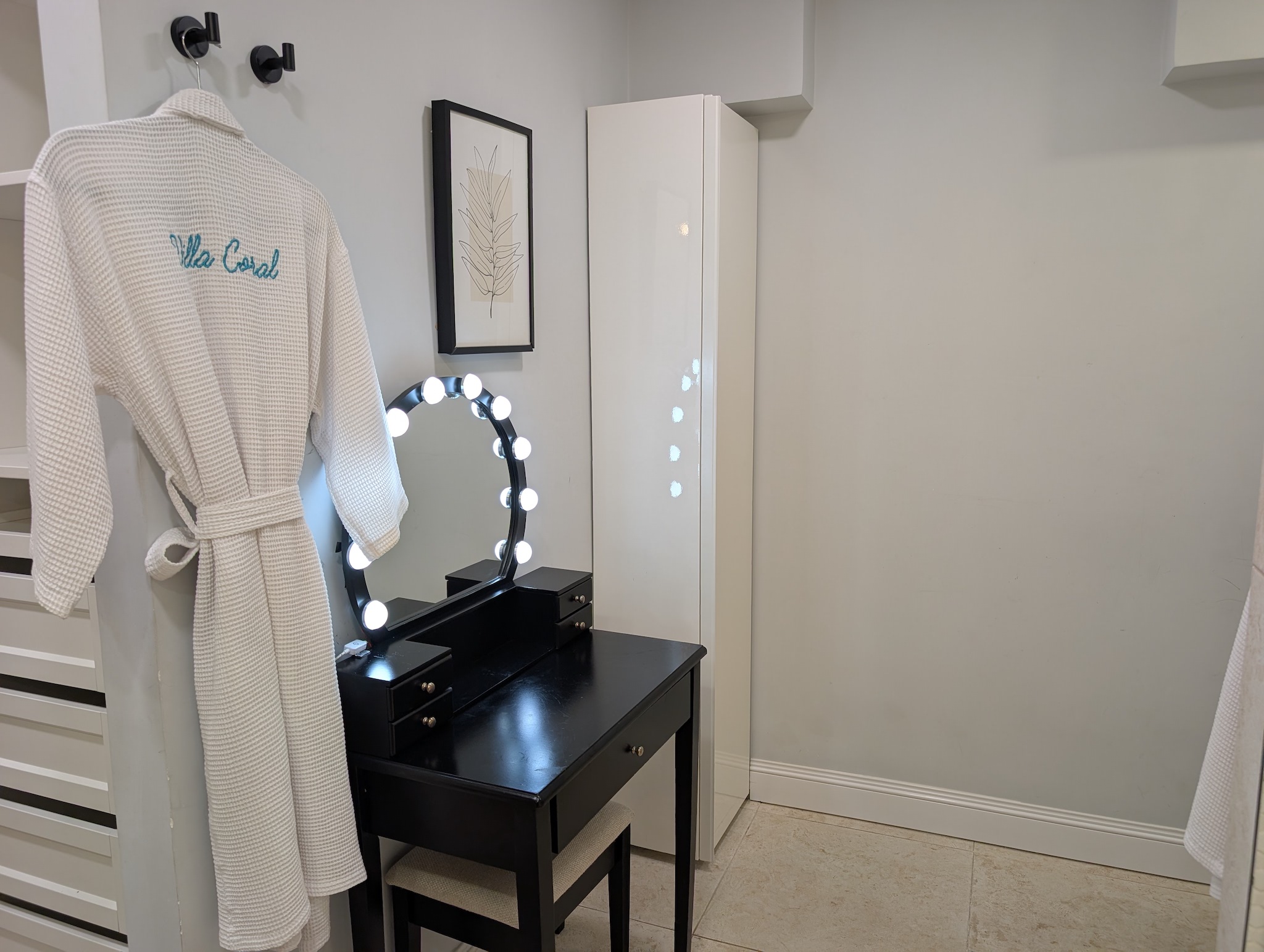 Dedicated black makeup vanity table with a lighted Hollywood mirror, matching chair, and a plush embroidered Villa Coral robe in the primary suite at Villa Coral in Dorado, Puerto Rico.
