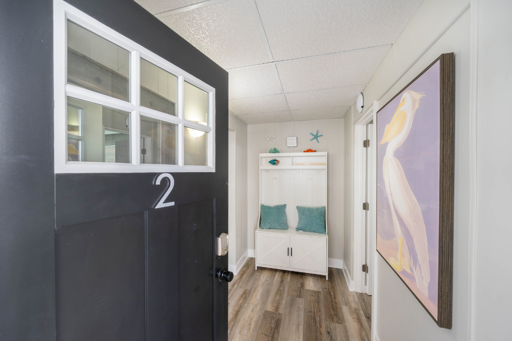Bright entry hallway with secure keypad access, wood-look flooring, and a built-in bench with hooks and storage. A practical drop zone for shoes, bags, and beach gear that keeps arrivals and departures easy and organized.