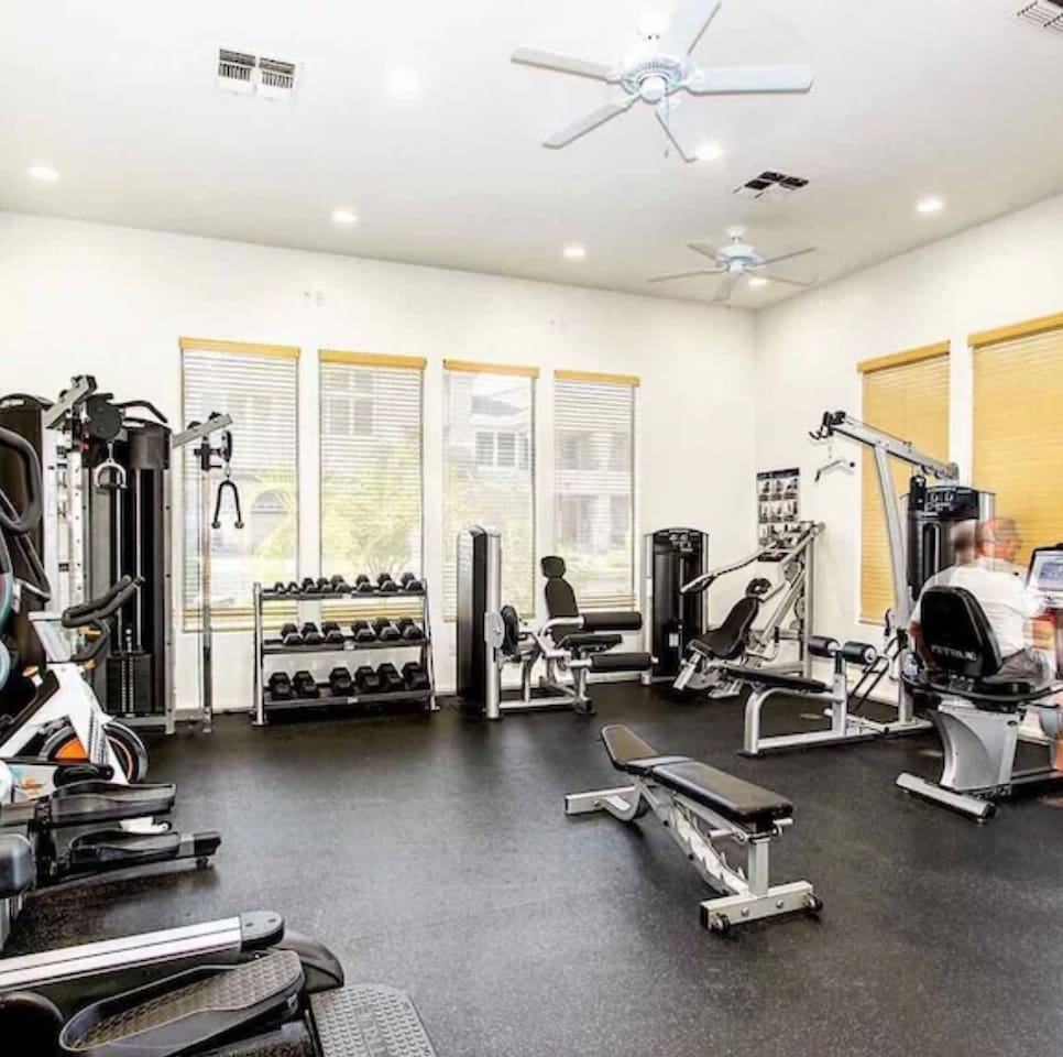 Shared fitness center with cardio machines, weight equipment, benches, and natural light for workouts during your stay.