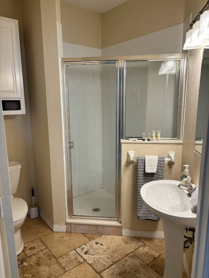 Bathroom with a shower enclosure, pedestal sink, and clean neutral finishes.