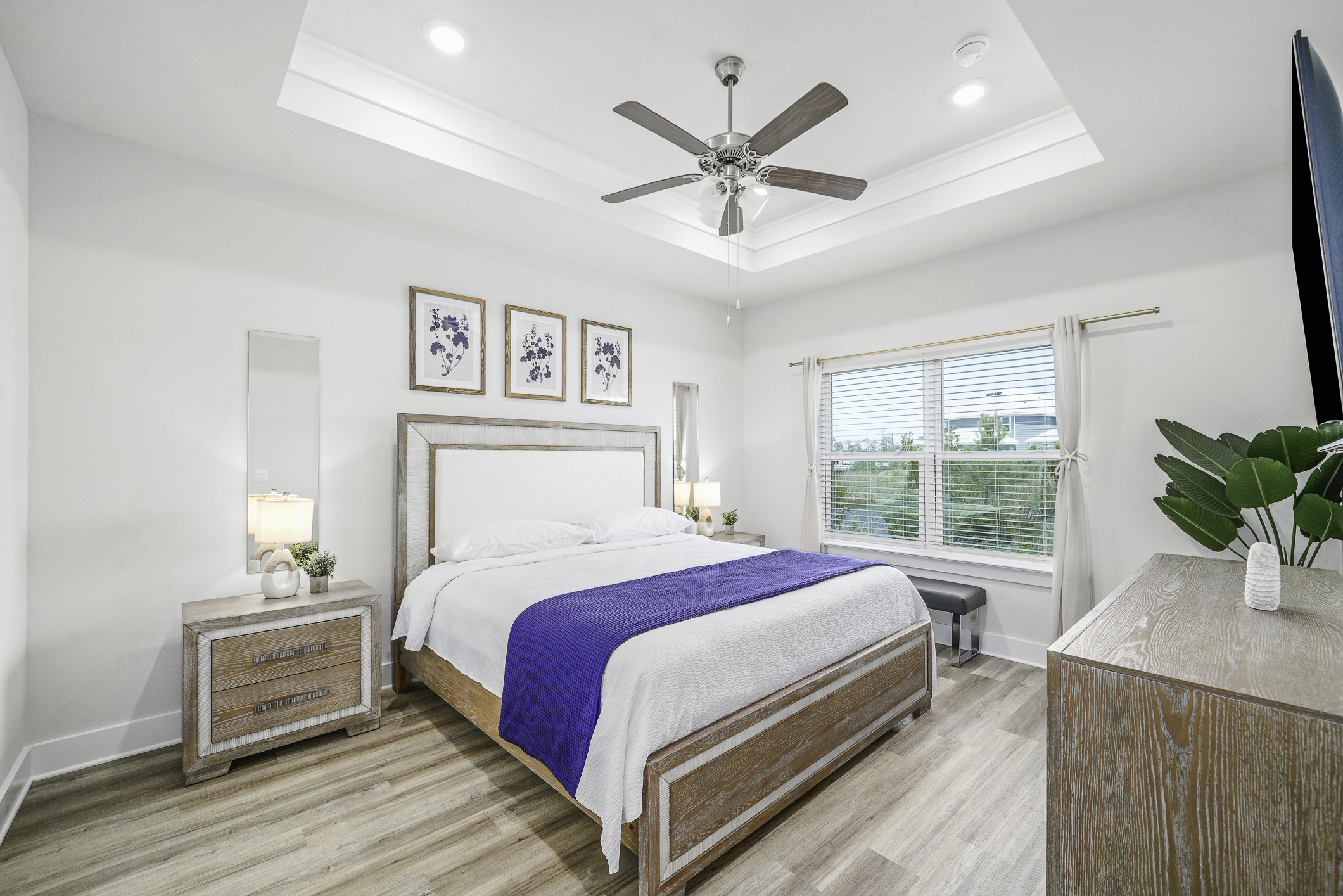 Primary Suite: Modern king bedroom featuring an en suite bathroom, plush linens, ceiling fan, elegant bedside lamps, dresser, and Smart TV.