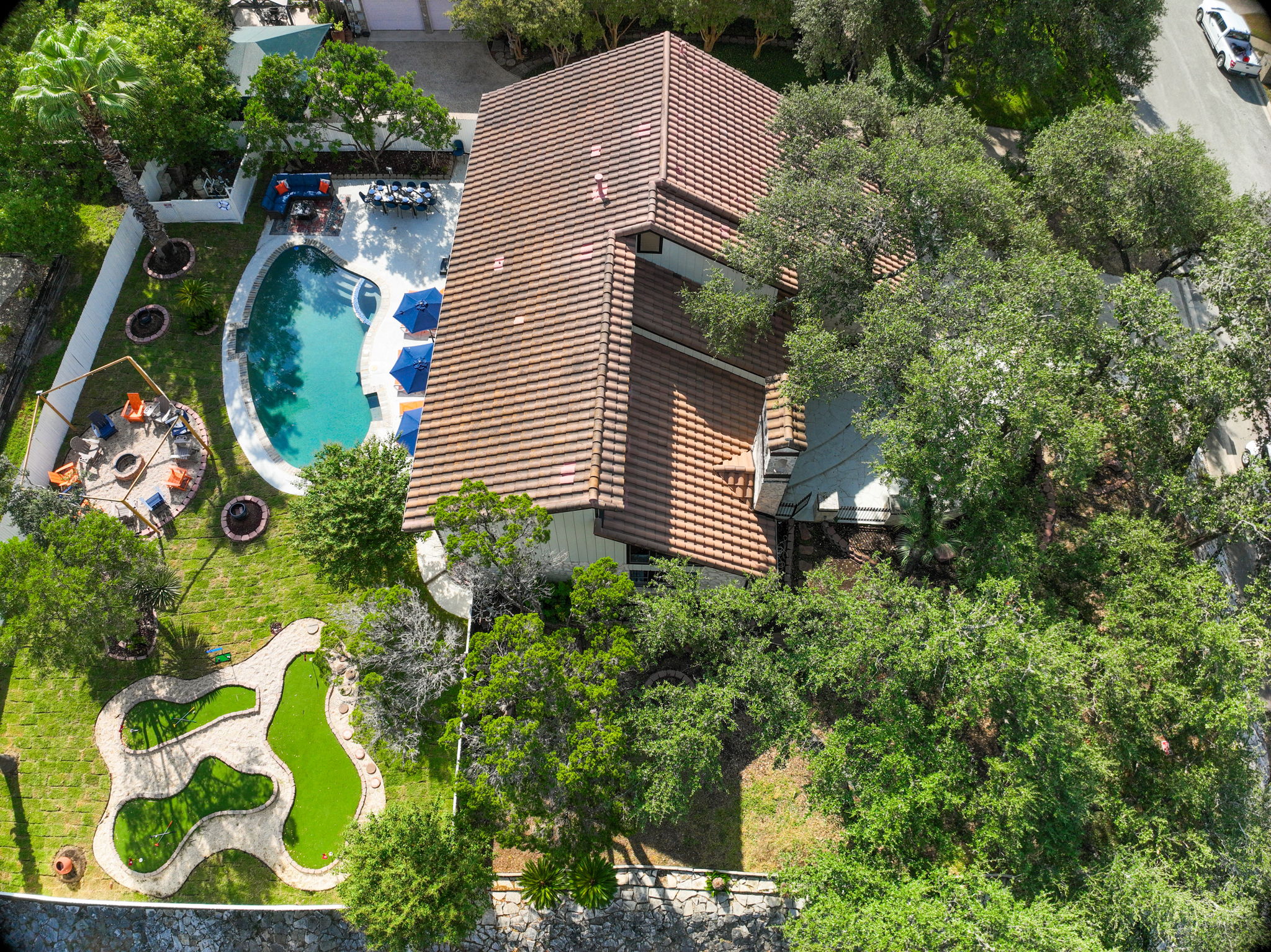 A stunning aerial of The Comfy Coyote. A spacious corner-lot retreat with lush trees framing the front lawn and a resort-style backyard complete with pool, mini golf, hot tub, and firepit.