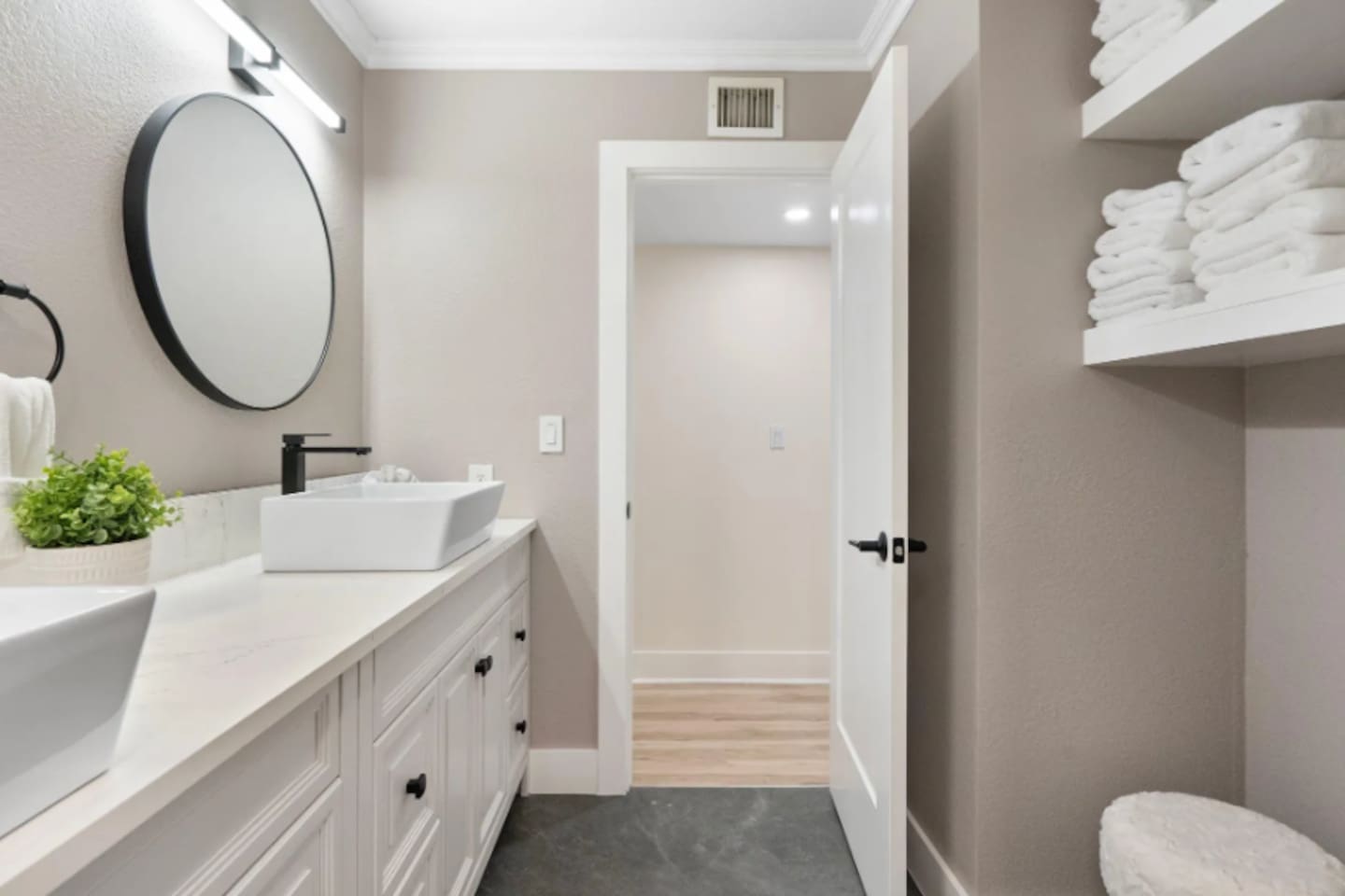 A crisp white vanity with a vessel sink and round mirror keeps things simple and bright, while open shelving means towels are always within reach.

