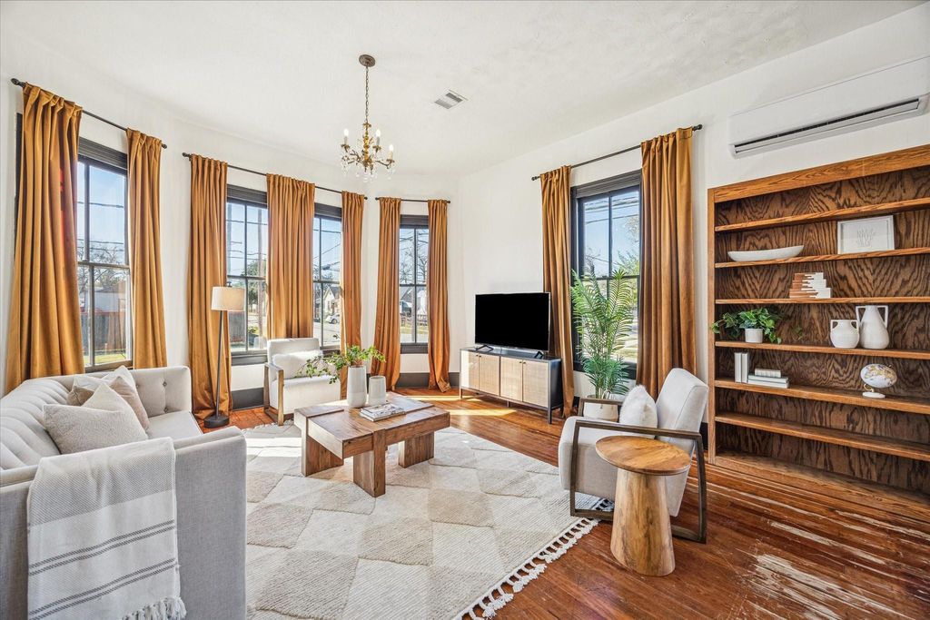 The living room makes a bold statement with rich original hardwood floors, tall windows that flood the space with natural light, and statement lighting, while an updated mini-split adds modern comfort without compromising the home’s vintage finishes.