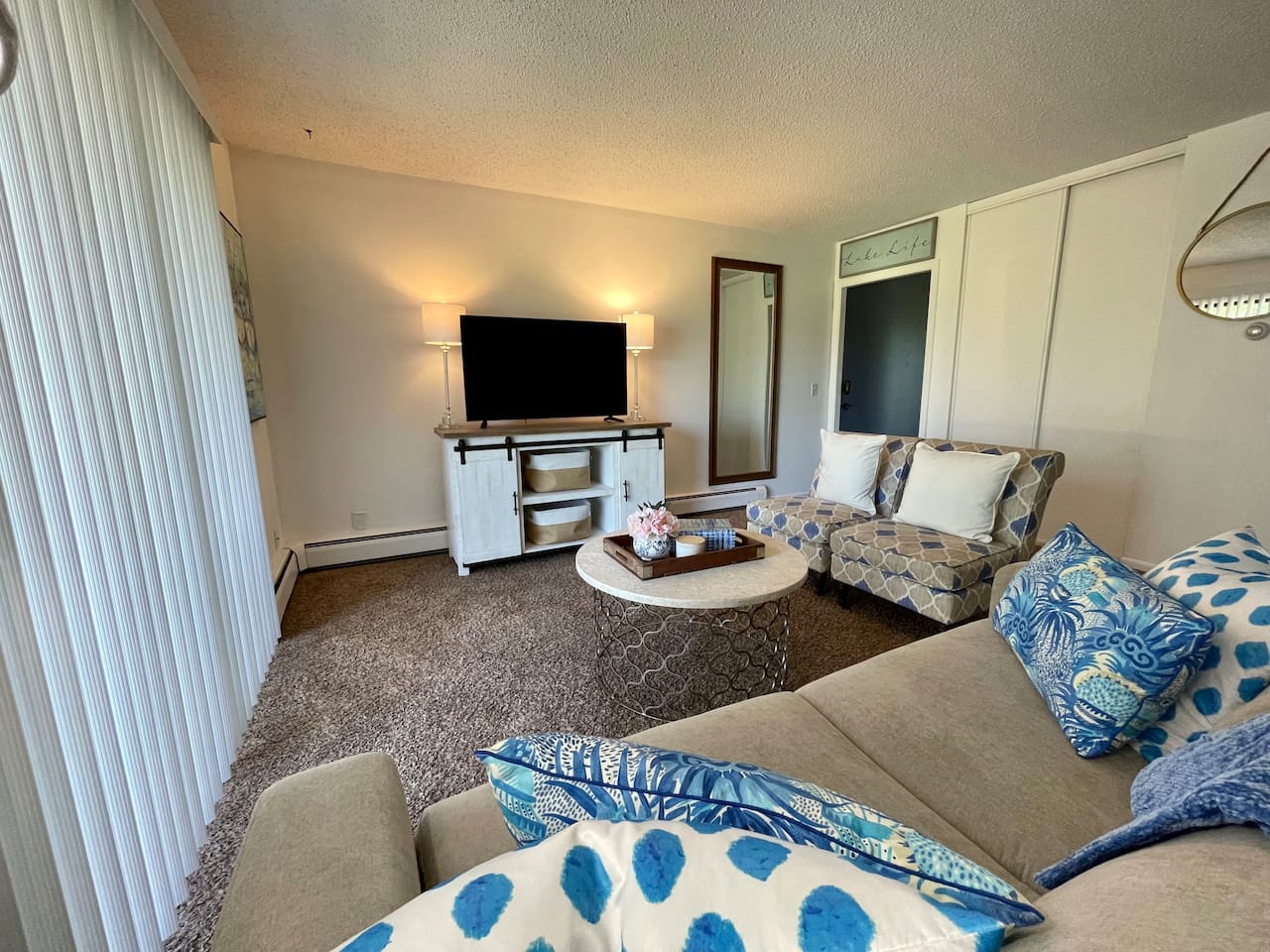 Bright and cozy living space with plush seating, calming blue accents, and a large smart TV for relaxing nights in. Natural light pours in through the sliding glass door, adding warmth to this charming retreat—perfect for comfort and convenience.