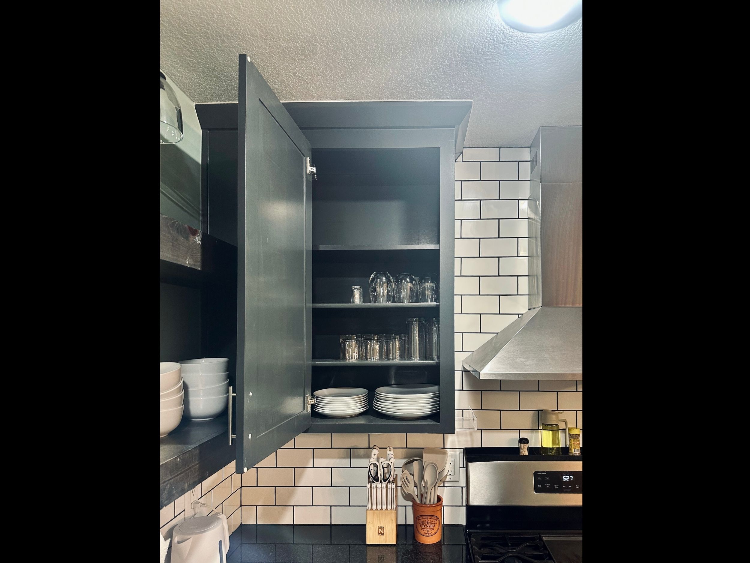 Kitchen cabinet stocked with drinking glasses, wine glasses, bowls, and plates for comfortable dining at home.