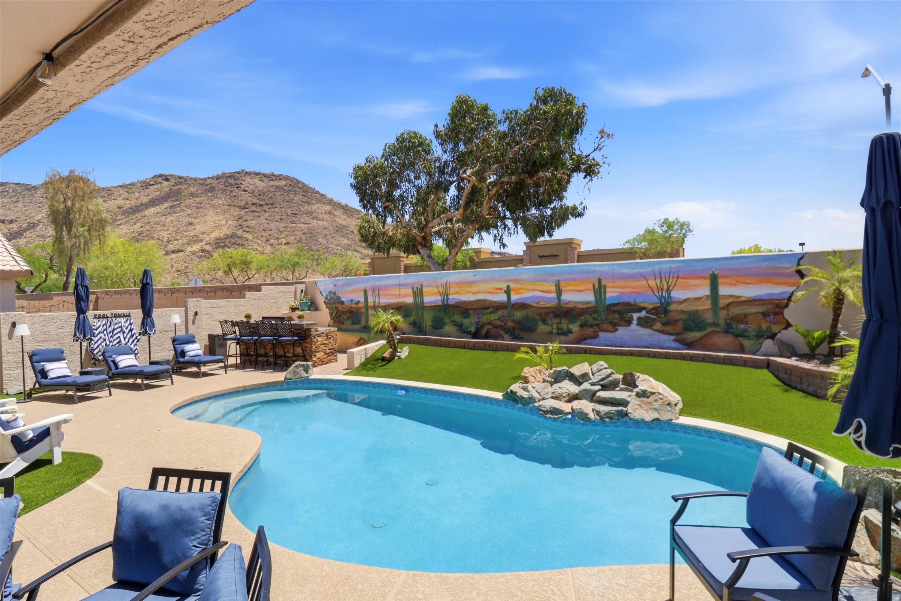 Private backyard pool with lounge seating, desert mural, mountain views, and open space for sunny outdoor relaxation.