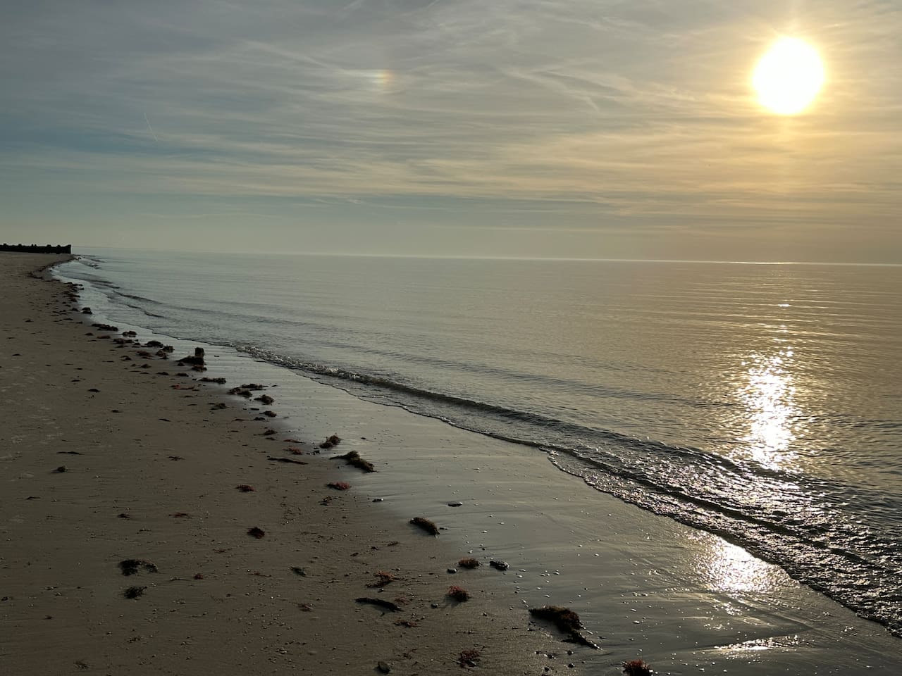 A serene and tranquil beach scene, where the sun reflects beautifully across the gentle, calm ocean waves. It is an ideal setting for enjoying a peaceful moment by the water.