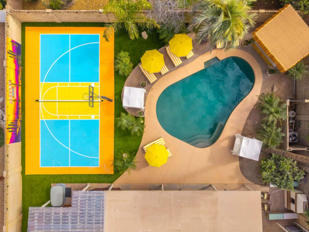 Overhead view of pool and sports court with yellow umbrellas and green landscaping—compact yet complete recreation space for guests.