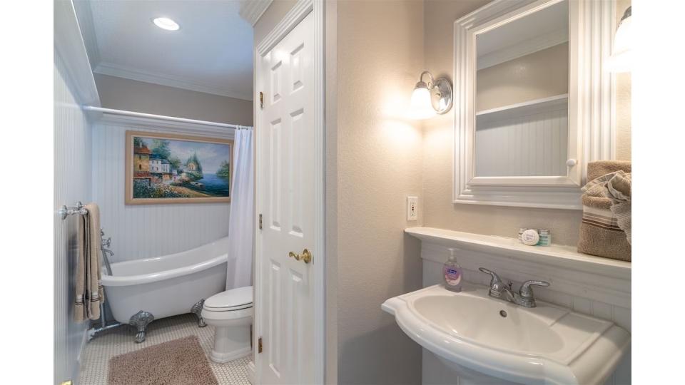 Ground-level King Master Suite Bath. Unwind in style in this charming bathroom featuring a classic clawfoot soaking tub—perfect for relaxing after days spent exploring the island. Coastal artwork and beadboard details add to the serene, spa-like atmosphere