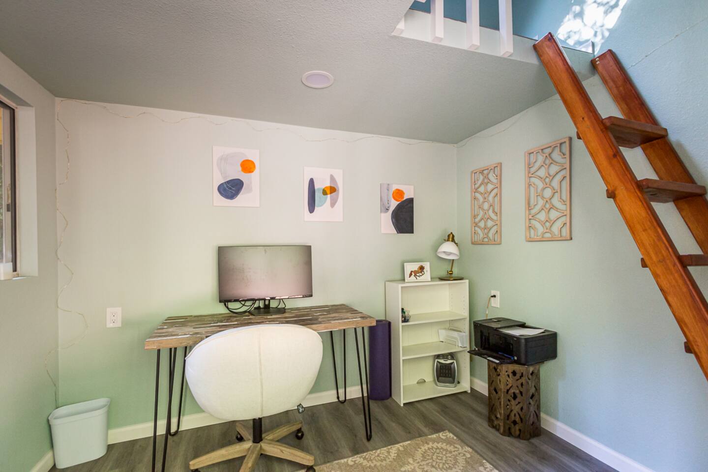 - Compact office space with desk, monitor, and modern decor
- Shelving and art pieces bring style and function to this work ready setup
- Wooden ladder leads to an upper loft area for added charm
