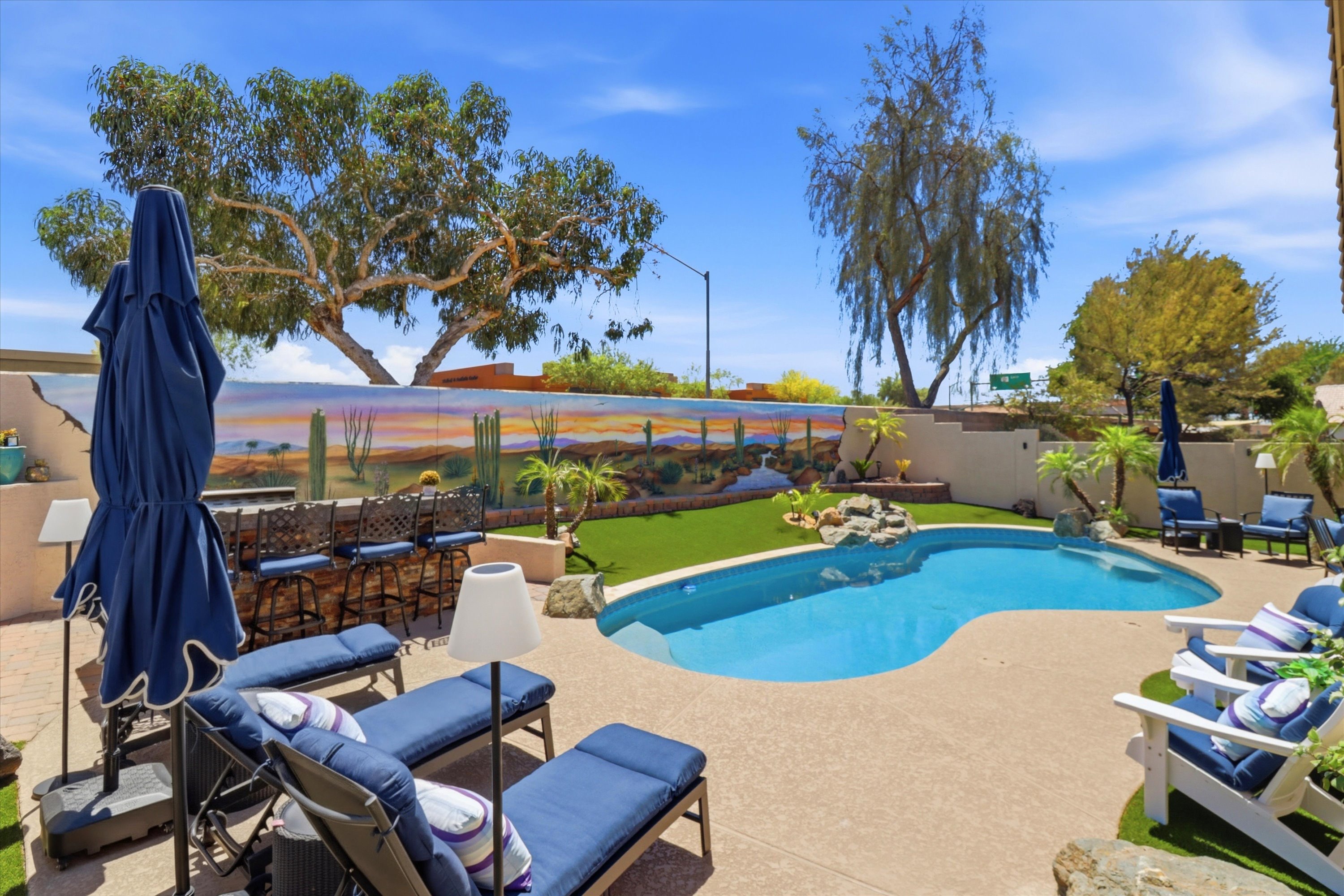 Private backyard pool with lounge seating, desert mural, mountain views, and open space for sunny outdoor relaxation.
