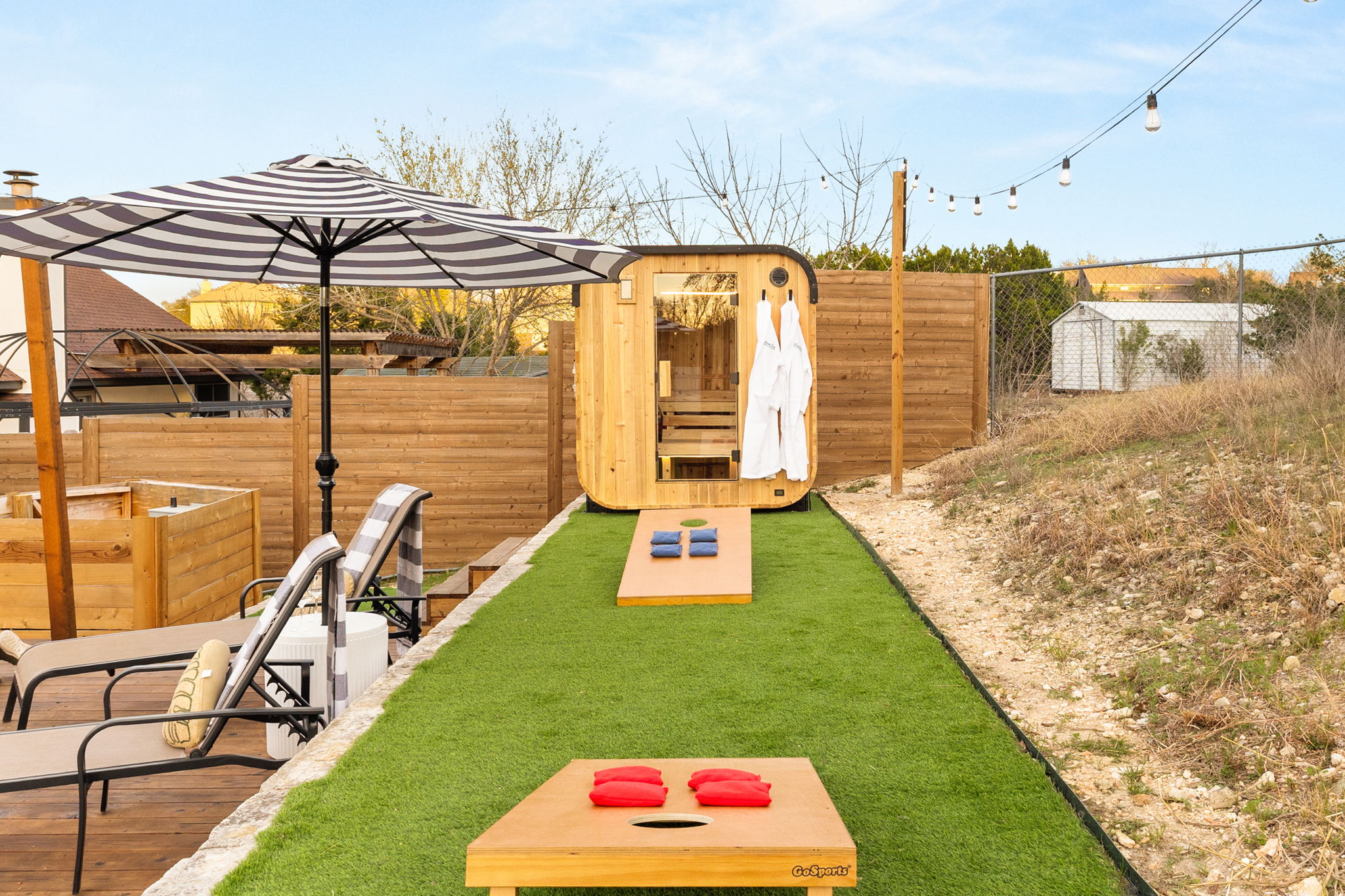 Game lawn with cornhole boards and a sauna backdrop: your backyard where wellness meets competition.