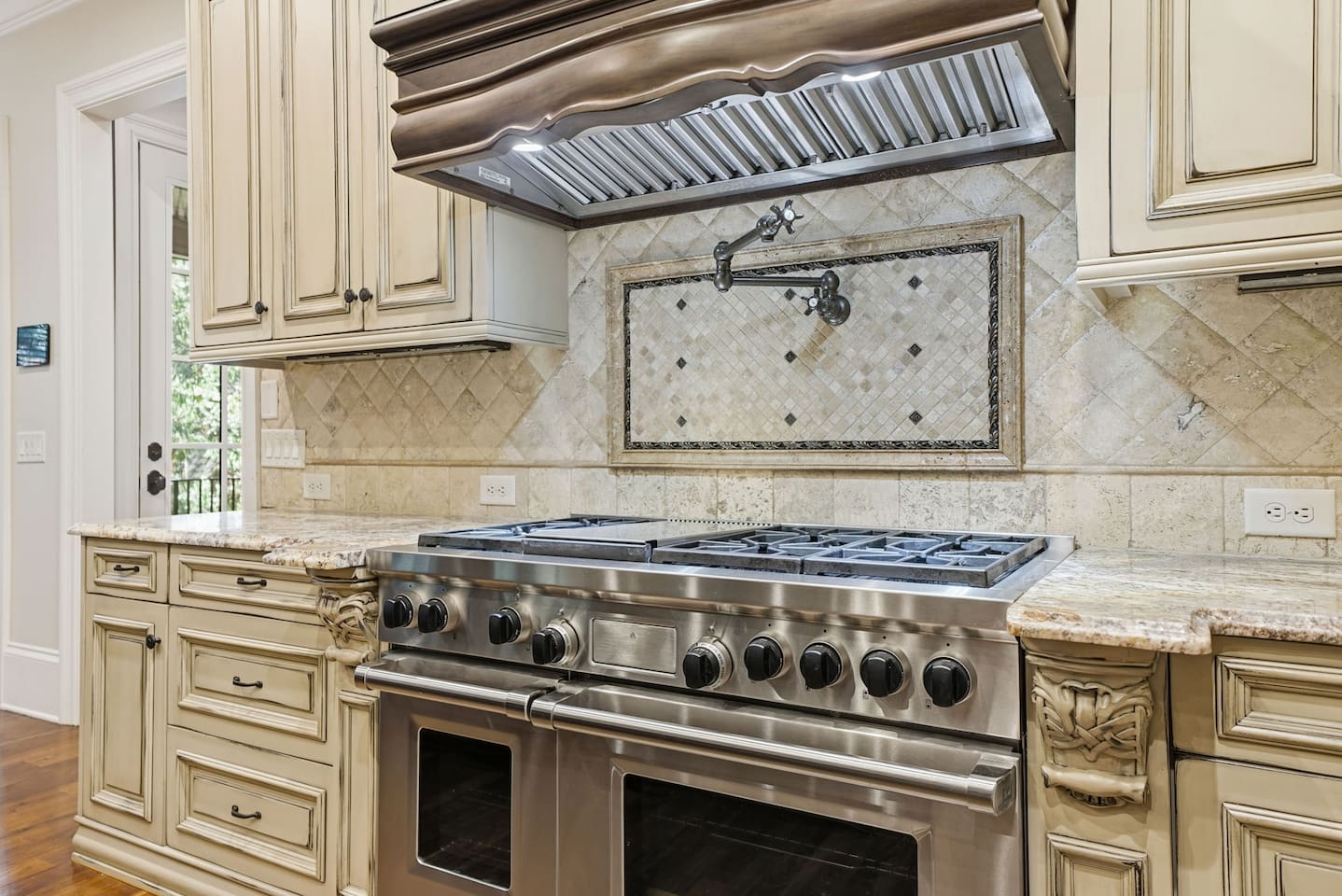 This open kitchen features beautiful cream wood cabinetry, sleek granite countertops, and an island that comfortably seats four. The bright, airy design makes it the perfect place to cook, gather, and share meals together.