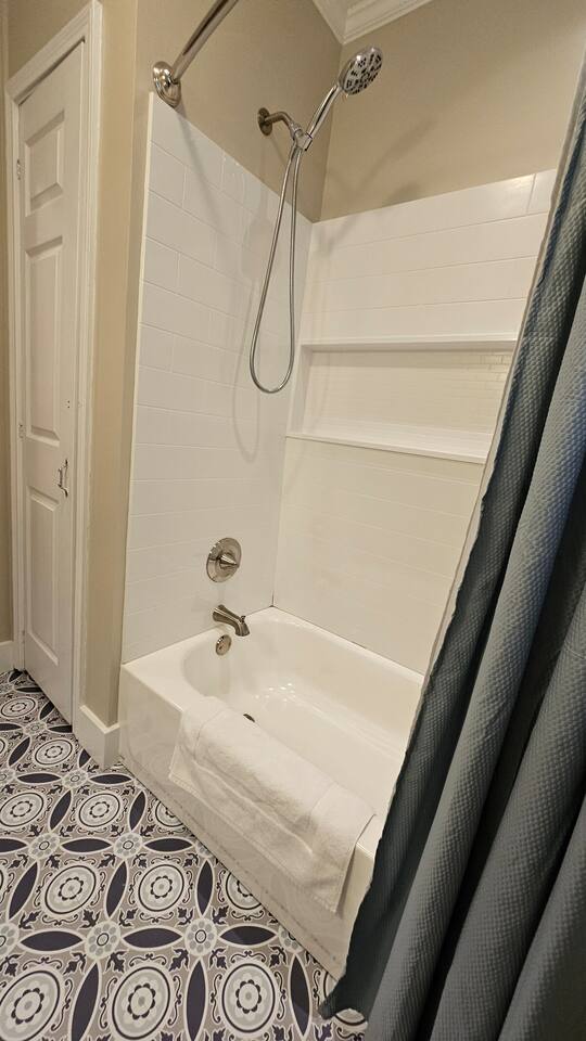 This bathroom features a clean and classic tub-shower combo with crisp white subway tile and built-in shelving, paired with a modern curved shower rod and a soft blue curtain. The patterned tile floor adds a bold, stylish contrast to the neutral tones.