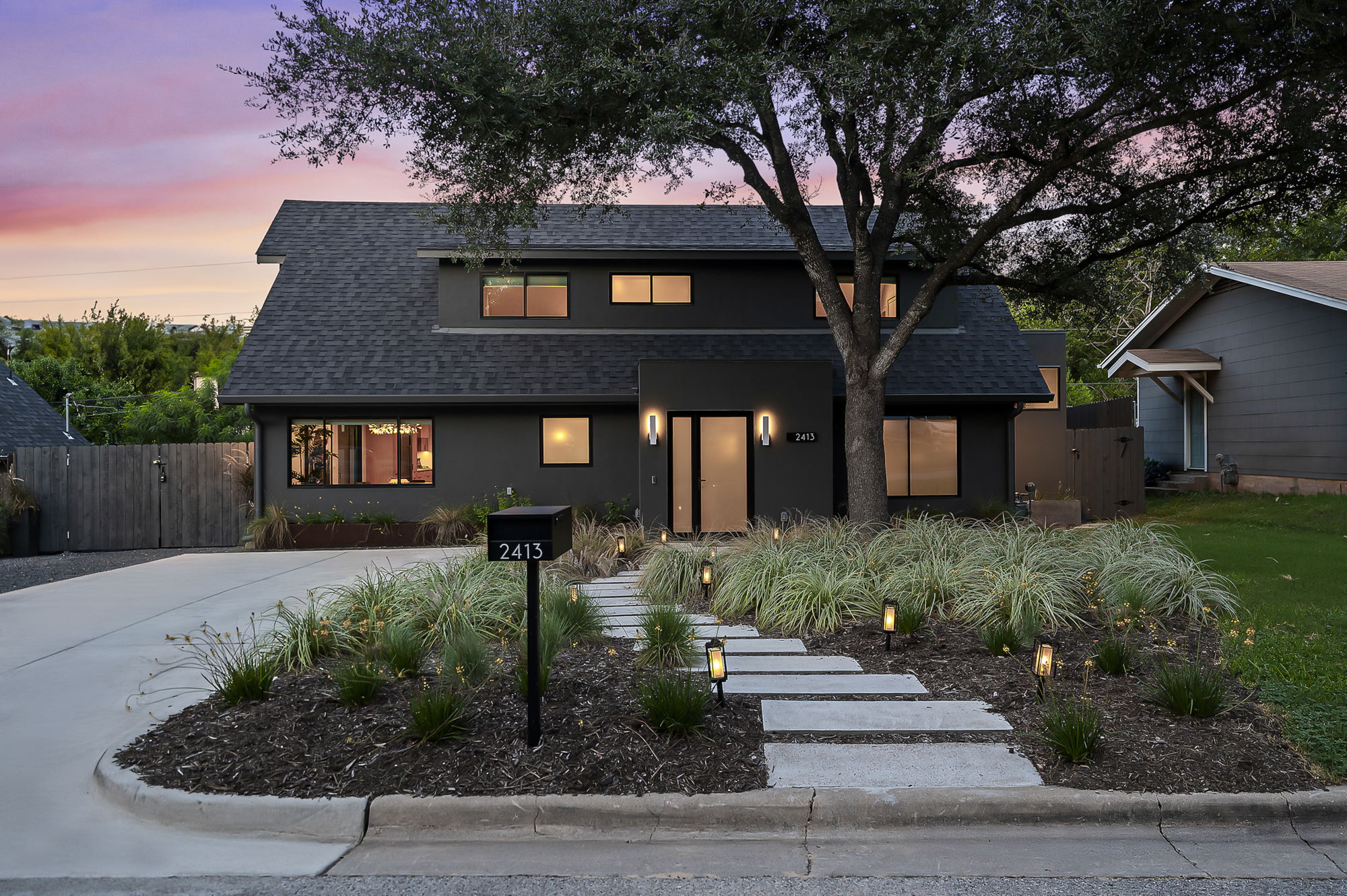 complemented by a beautifully manicured front yard featuring a meandering stone walkway, lush grasses, and accent lighting that creates a welcoming glow at dusk.