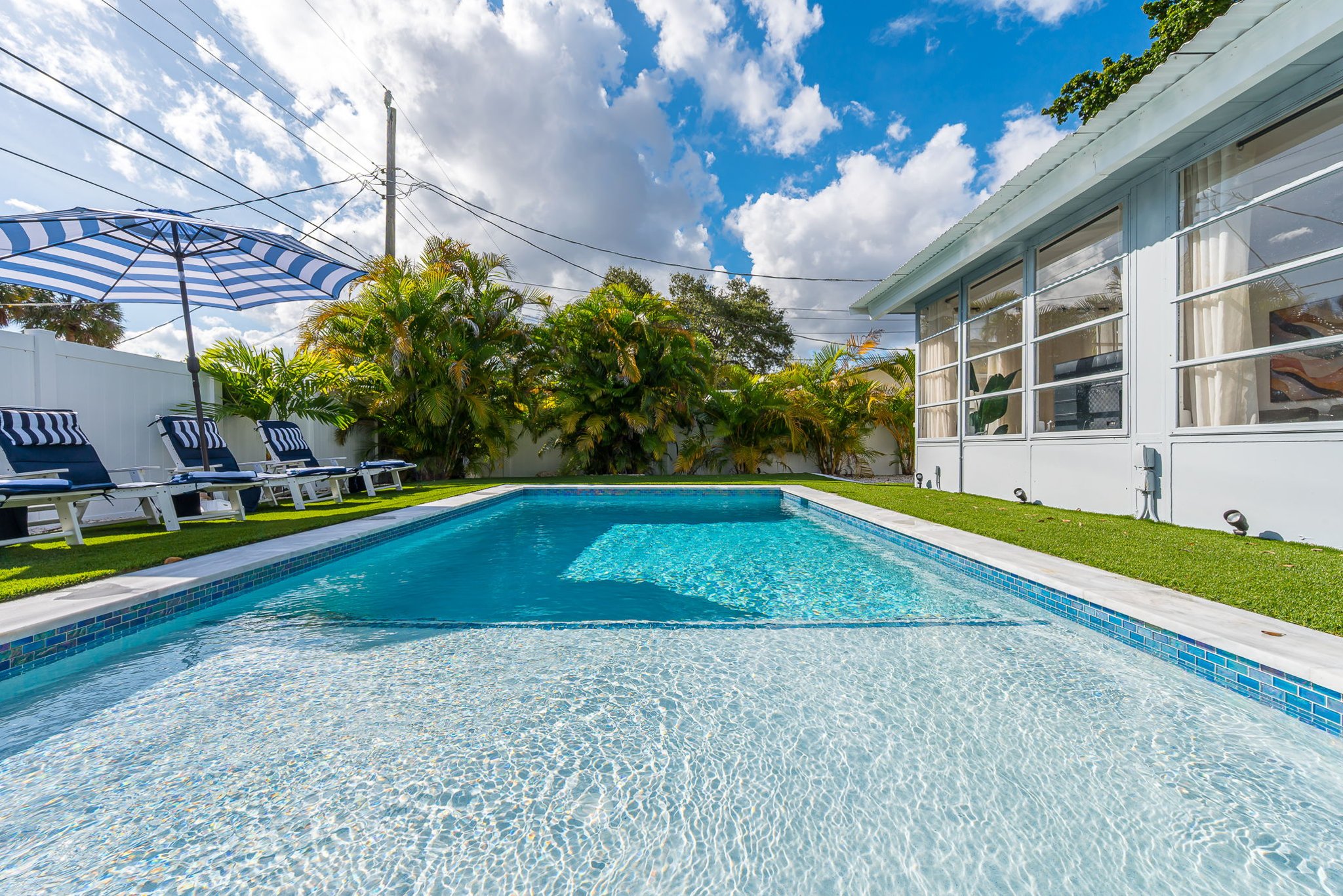 Dive into luxury with a sparkling heated saltwater pool, surrounded by lush palms, chic loungers, and modern turf for the perfect resort-style backyard escape.