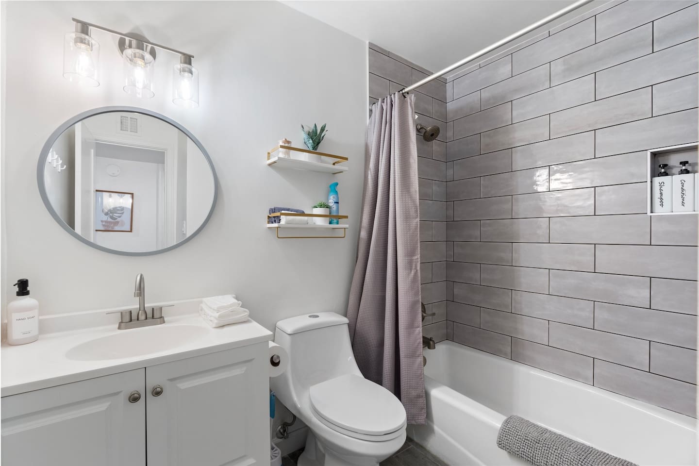 Enjoy a clean and modern space with sleek gray tile, a rainfall showerhead, built-in shampoo dispensers, and thoughtful touches like floating shelves and plush towels.