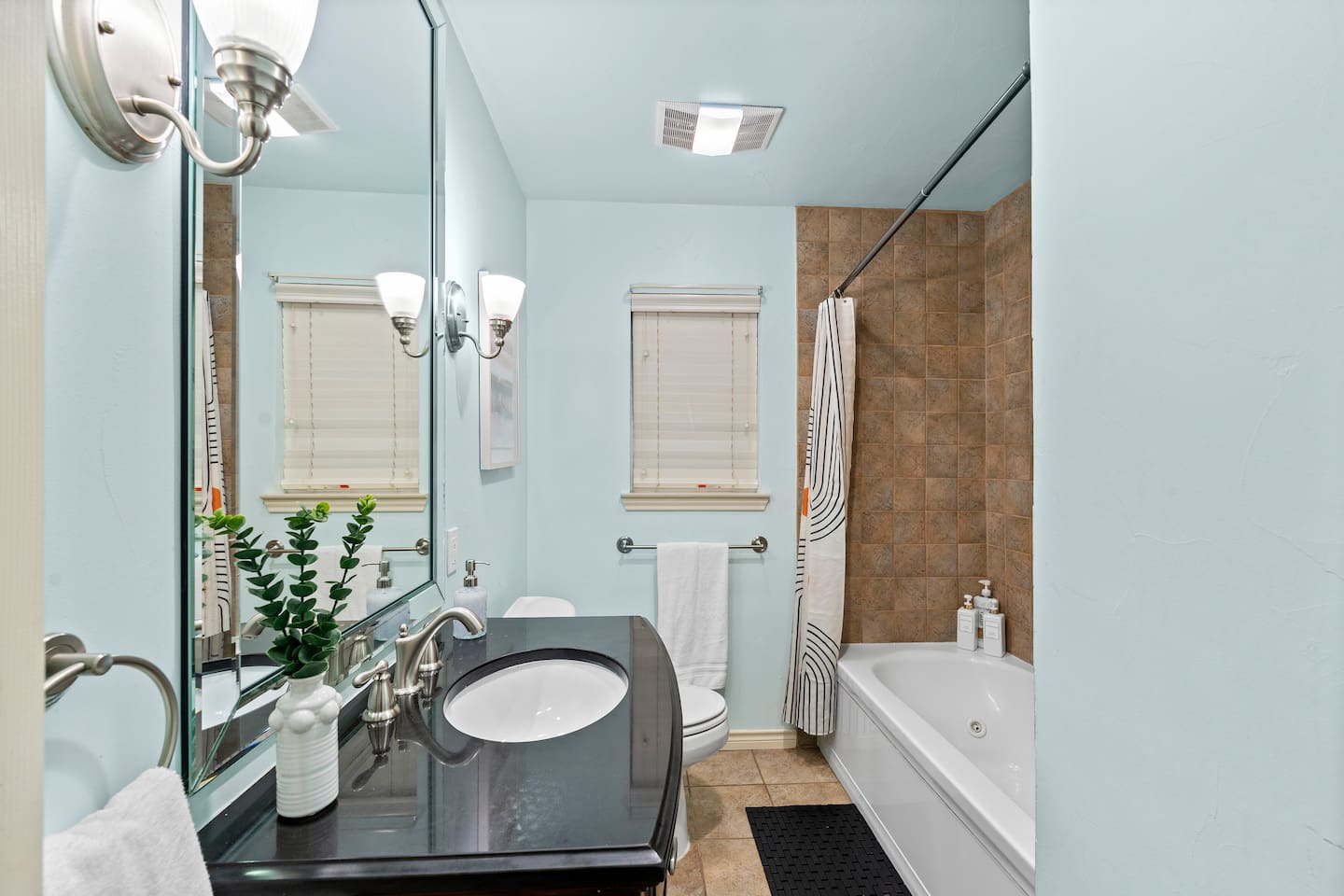 This modern bathroom features dual lighting, a granite vanity, and calming blue walls to elevate your morning routine.