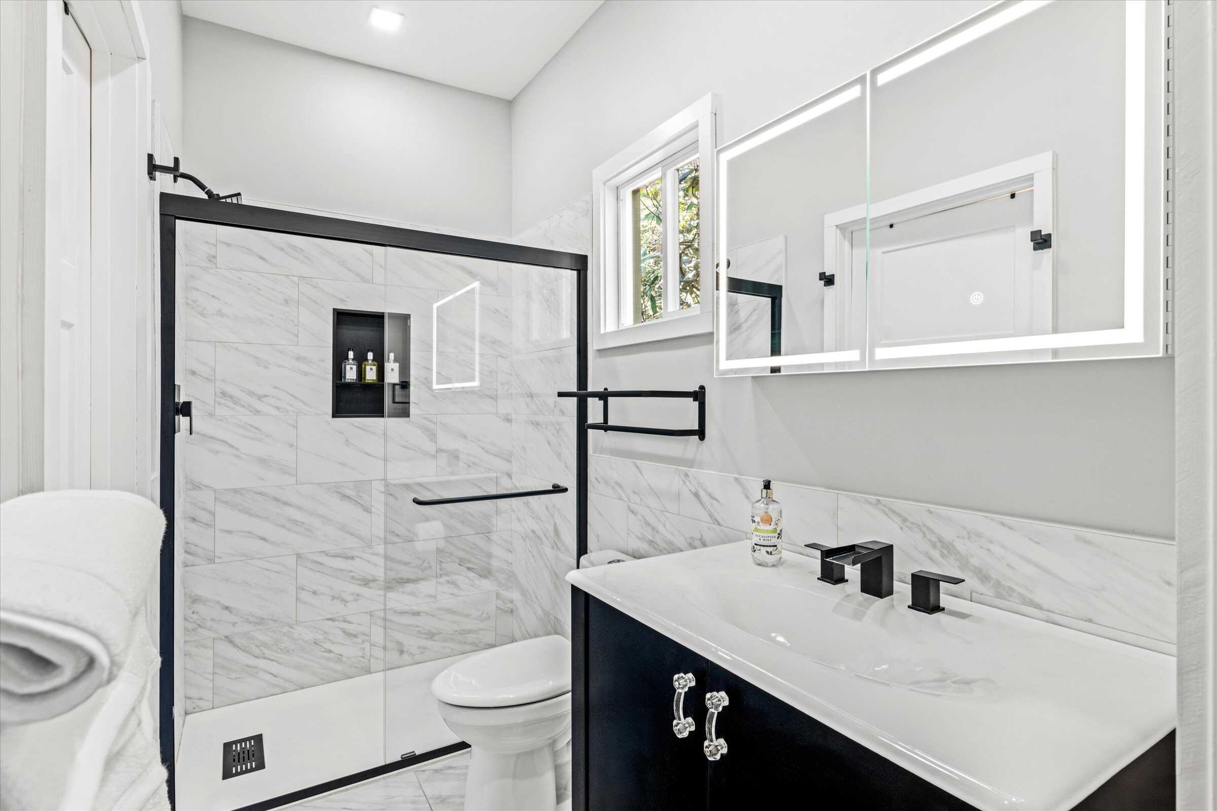 Guest bathroom with marble tile shower and flooring. LED lighted mirror above sink.