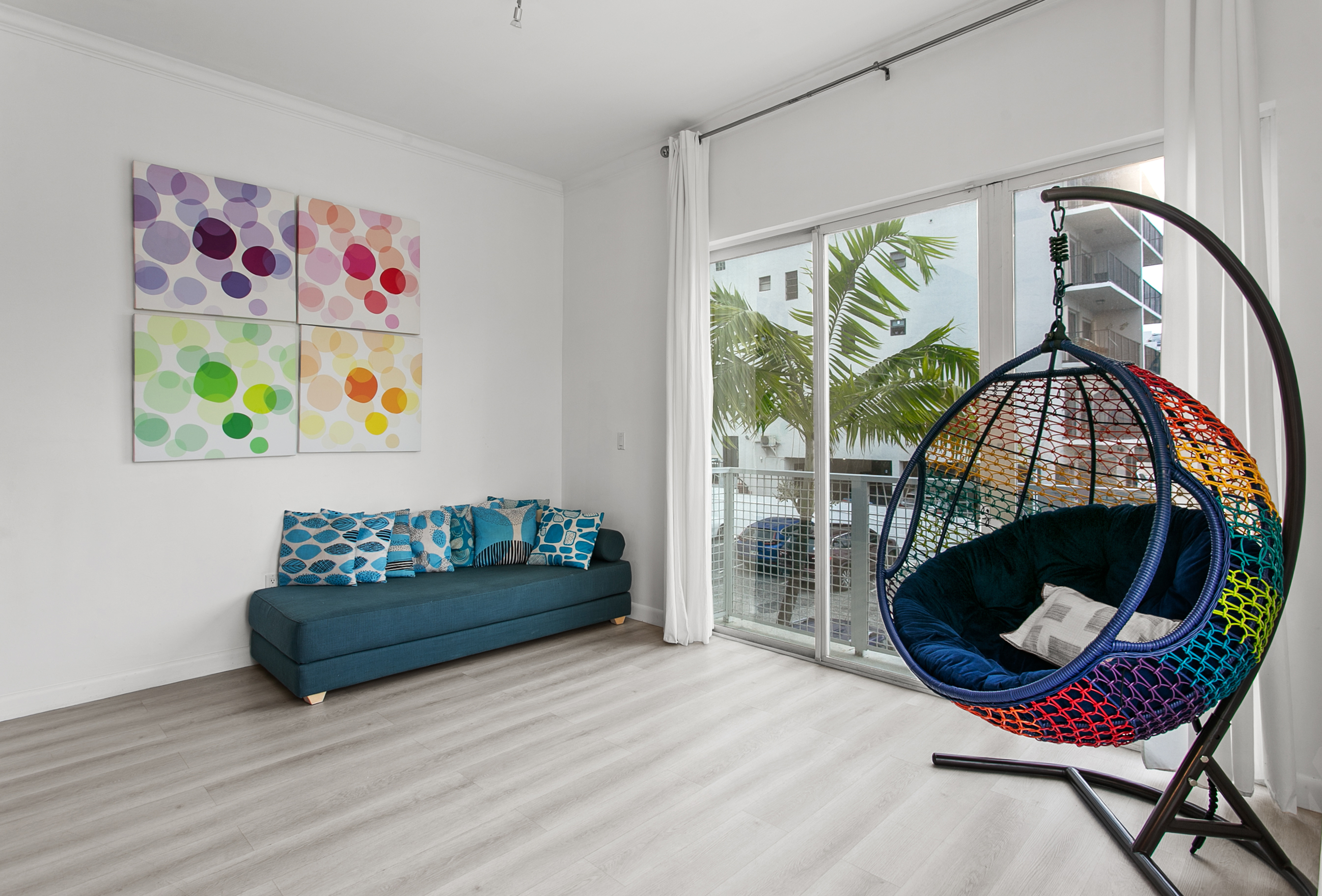 Huge sunny corner living room with two sofas, a daybed, and a swing chair. Private balcony with city and waterway views.