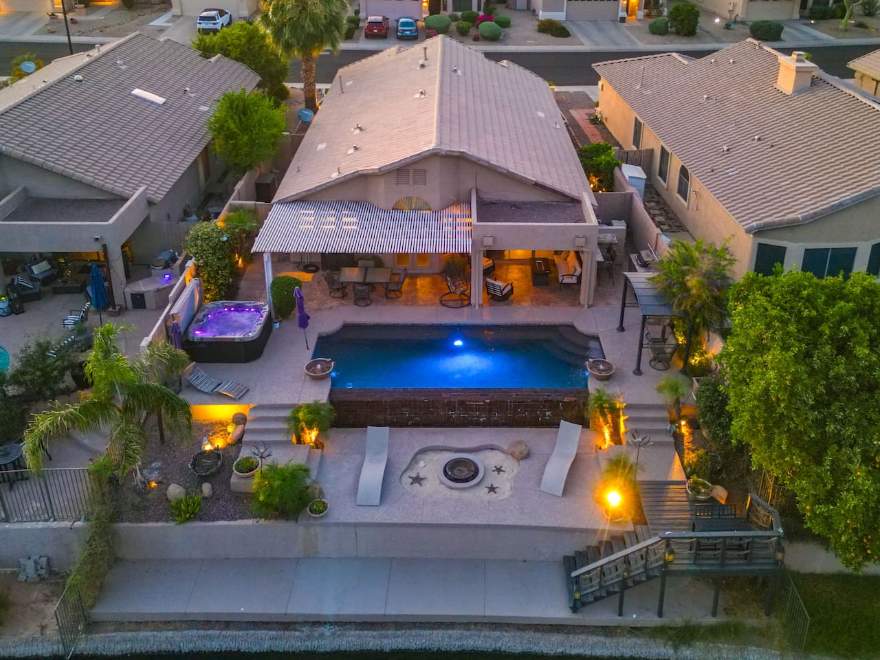 An aerial view reveals just how much this backyard has to offer — a private pool, hot tub, covered patio, fire pit, and direct lake access, all in one stunning outdoor retreat.