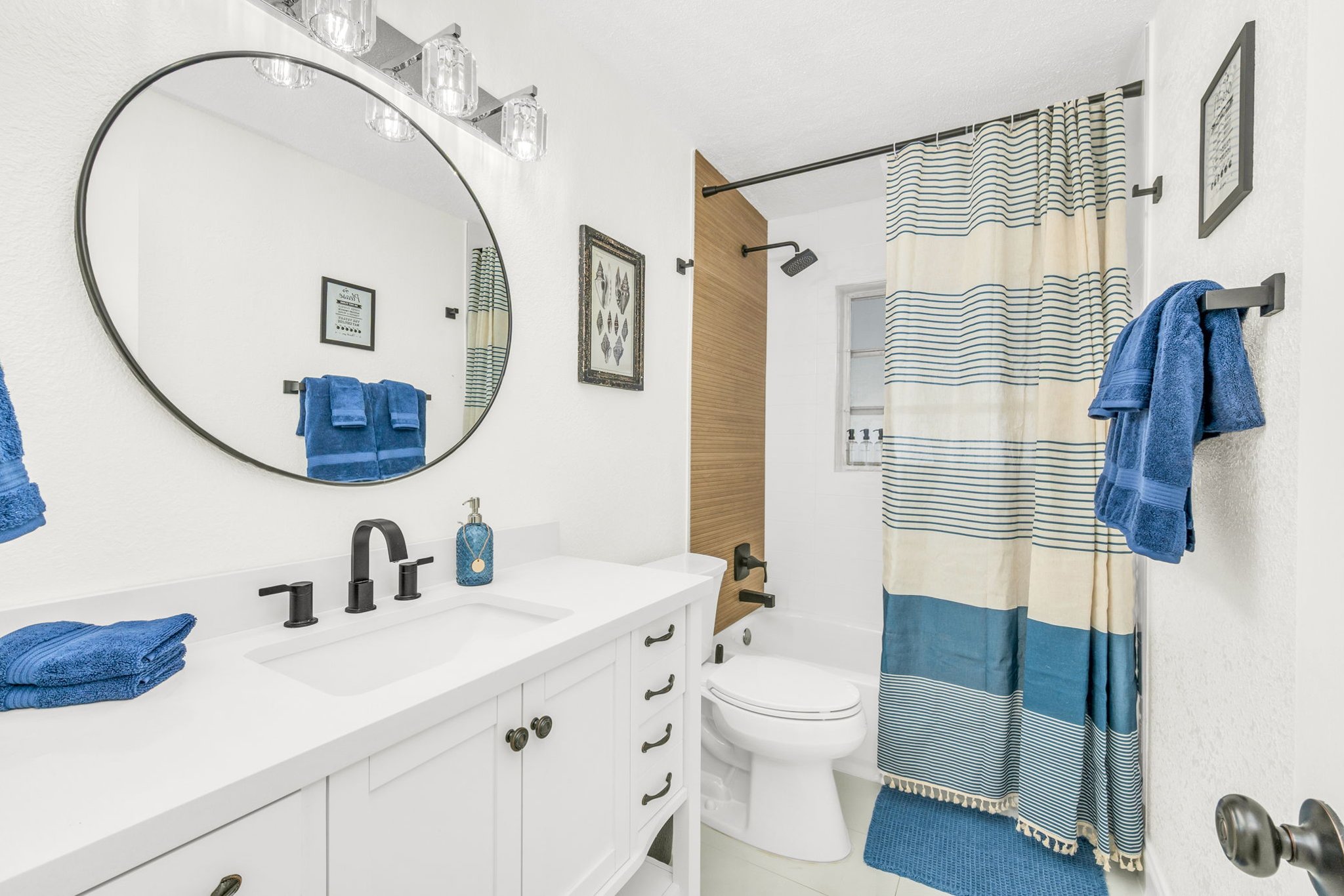 This beautifully updated guest bathroom showcases a modern vanity, black matte hardware, a chic shower/tub combination, and calming blue tones throughout.