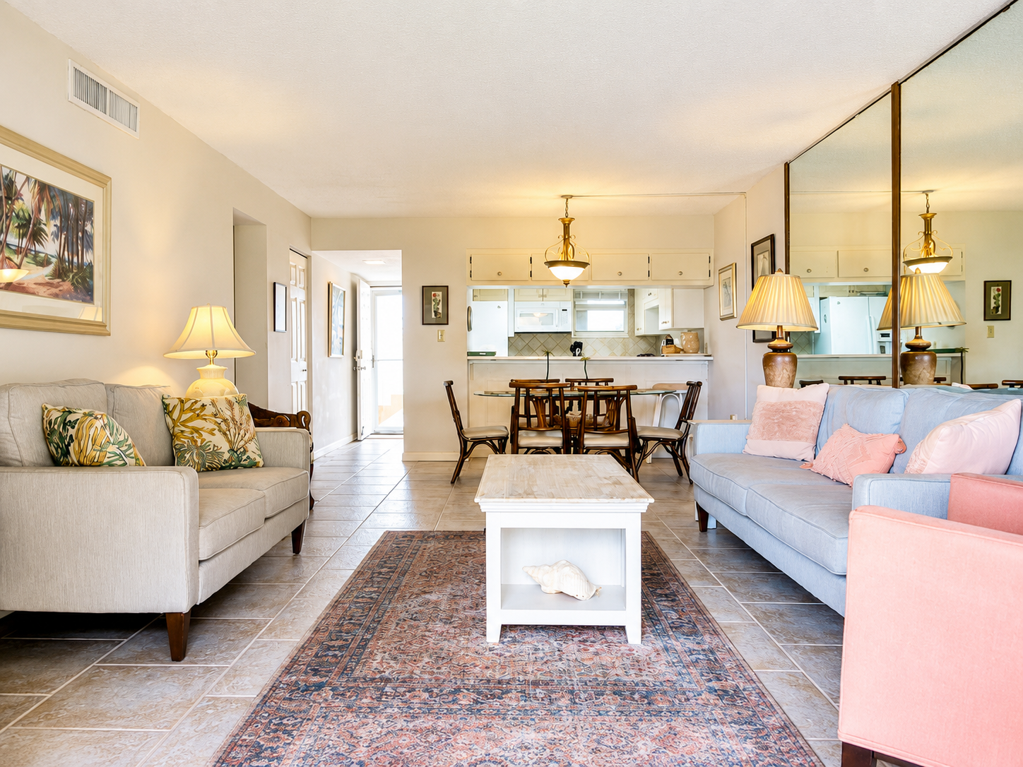 Bright living room with beige and blue sofas, patterned rug, and open kitchen.