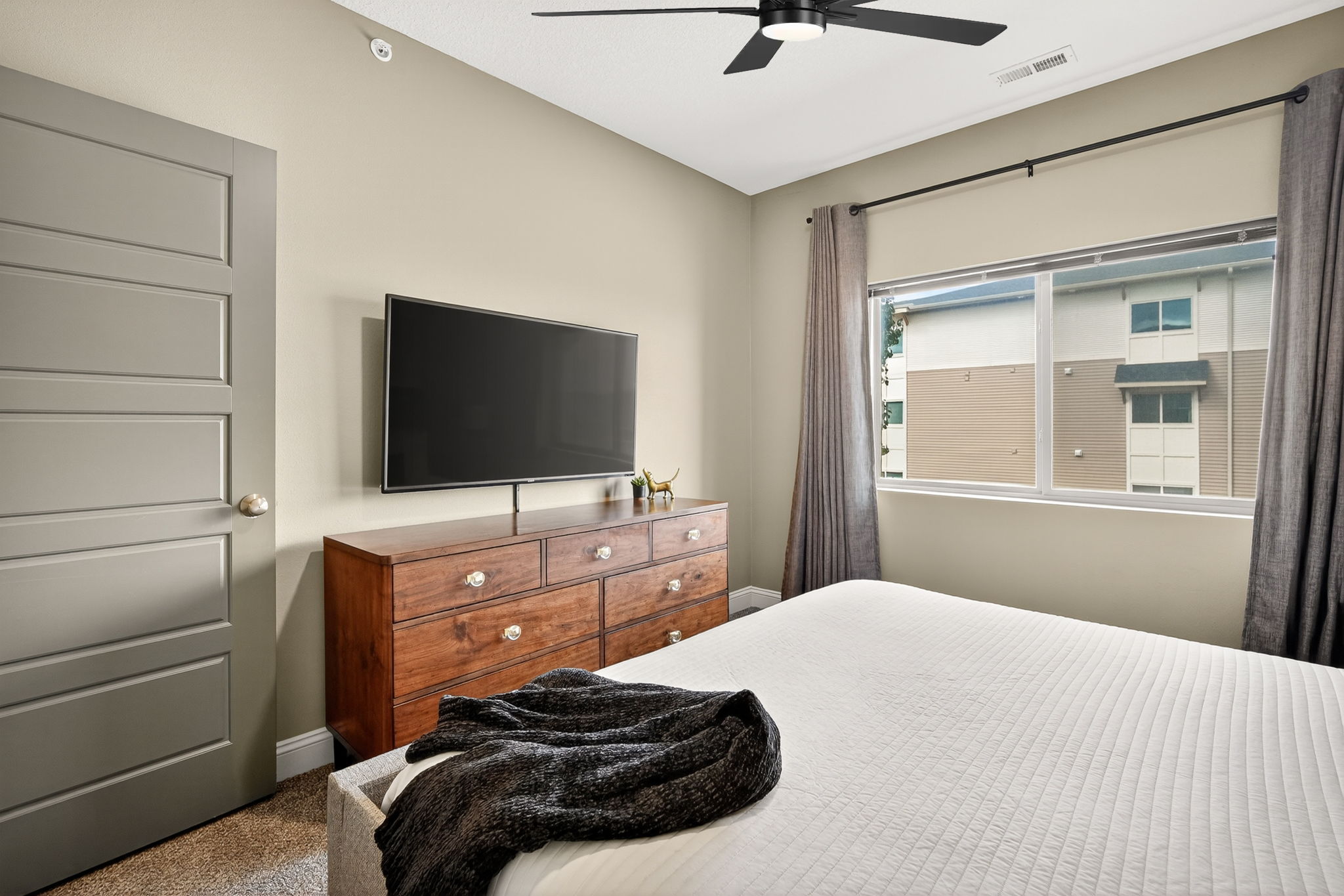 Bedroom retreat featuring a 55" smart TV, sleek dresser, blackout curtains, ceiling fan and stylish décor for a condo-inspired stay.