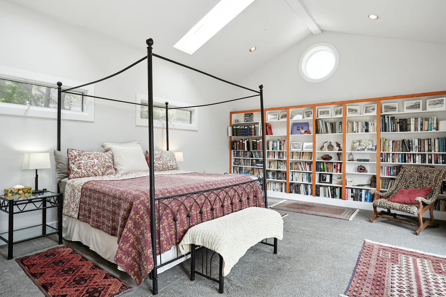 - Airy bedroom with four poster king bed, patterned bedding, and cozy bench at foot  
- Wall to wall bookshelves stocked with reading selections for a relaxing stay  
- Skylights and round window fill the space with soft natural daylight