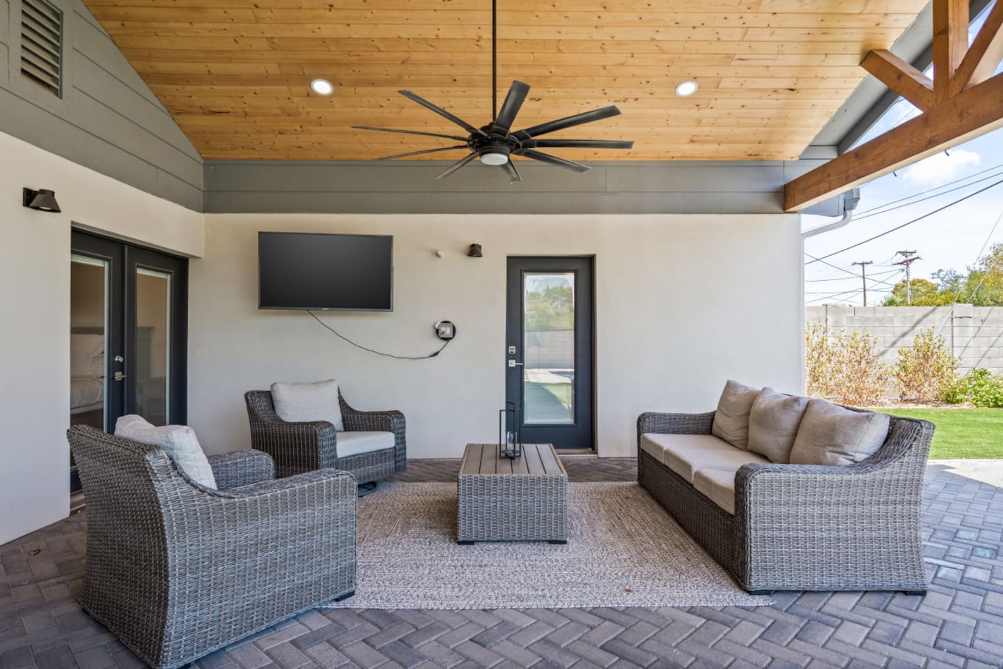 Covered patio lounge with outdoor seating, TV, and ceiling fan for comfortable backyard downtime.