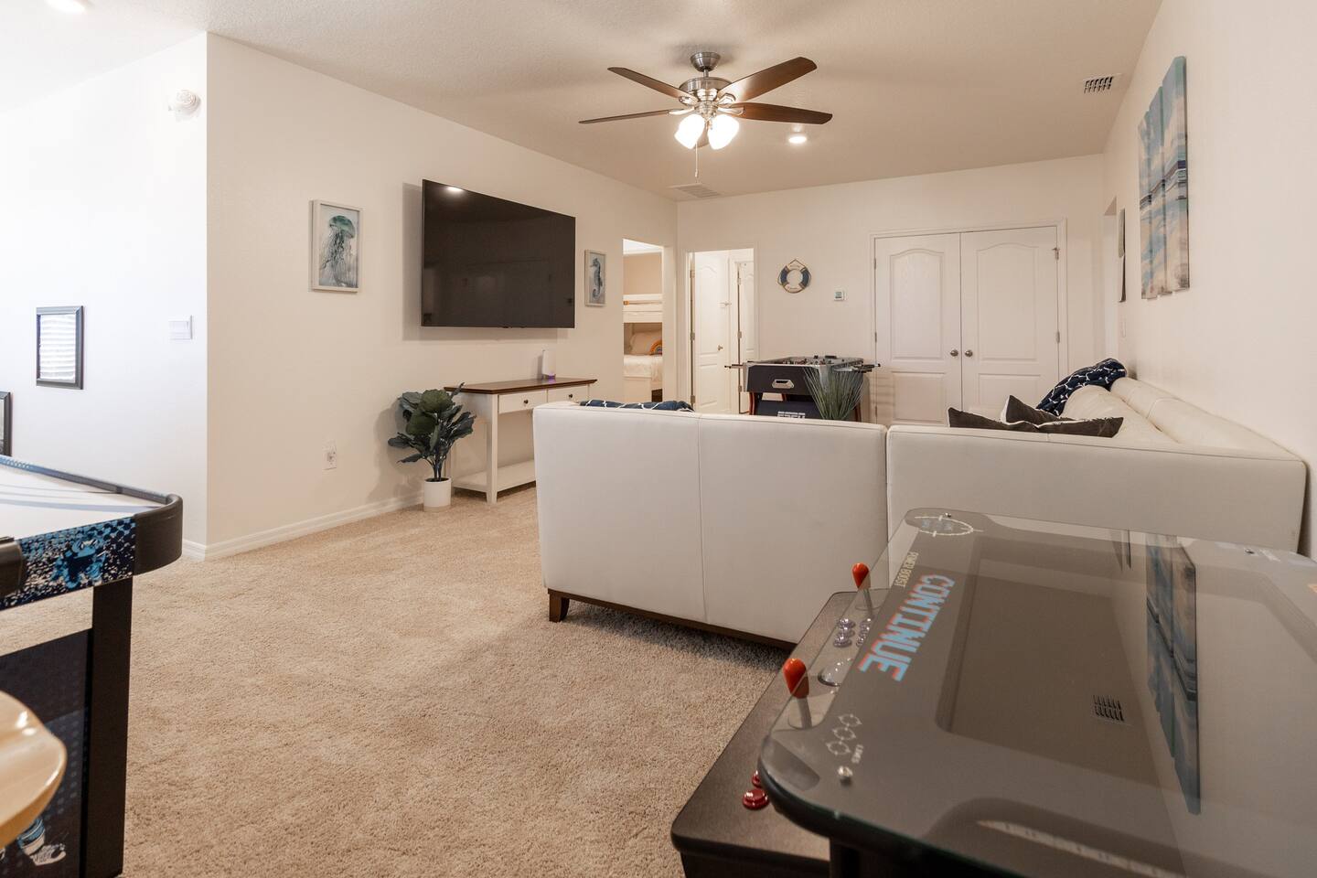 Upstairs lounge area with couch, 75in smart TV, overhead fan, air hockey table, foosball table and two player arcade game with thousands of games. 