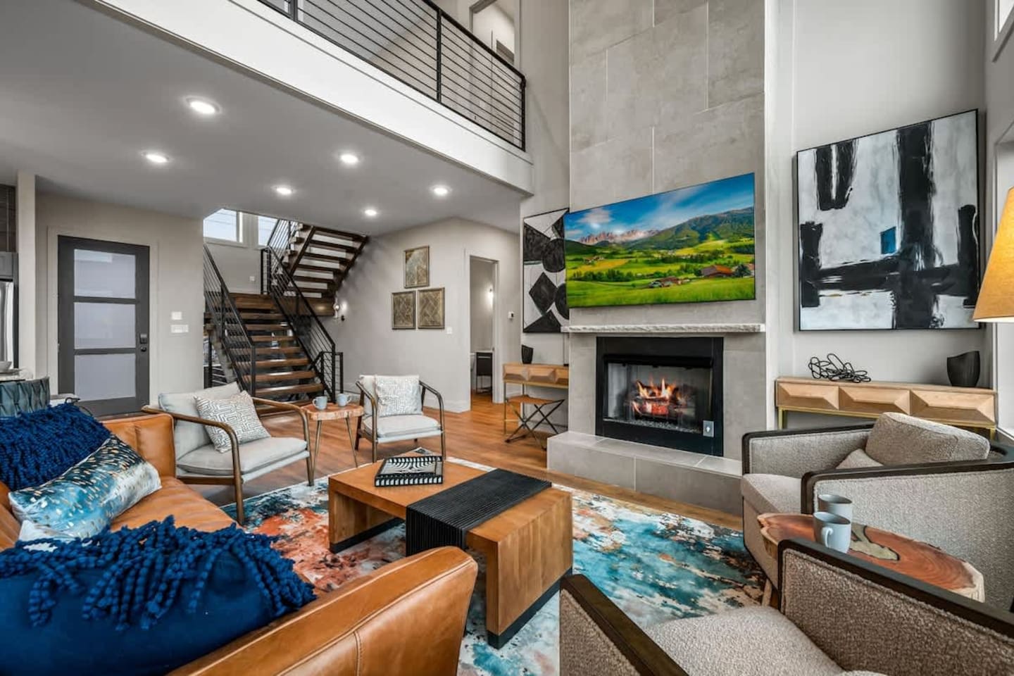 Elegant Gatlinburg cabin living room with large stone fireplace, floor-to-ceiling windows, and open staircase linking upper and lower levels. Bright, airy space with breathtaking Smoky Mountain views. Perfect luxury retreat for families or groups.