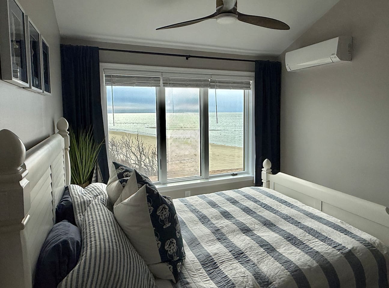 This serene bedroom features a white bed frame dressed in blue-striped bedding. The room includes dark curtains framing a window that offers beautiful, direct water views.