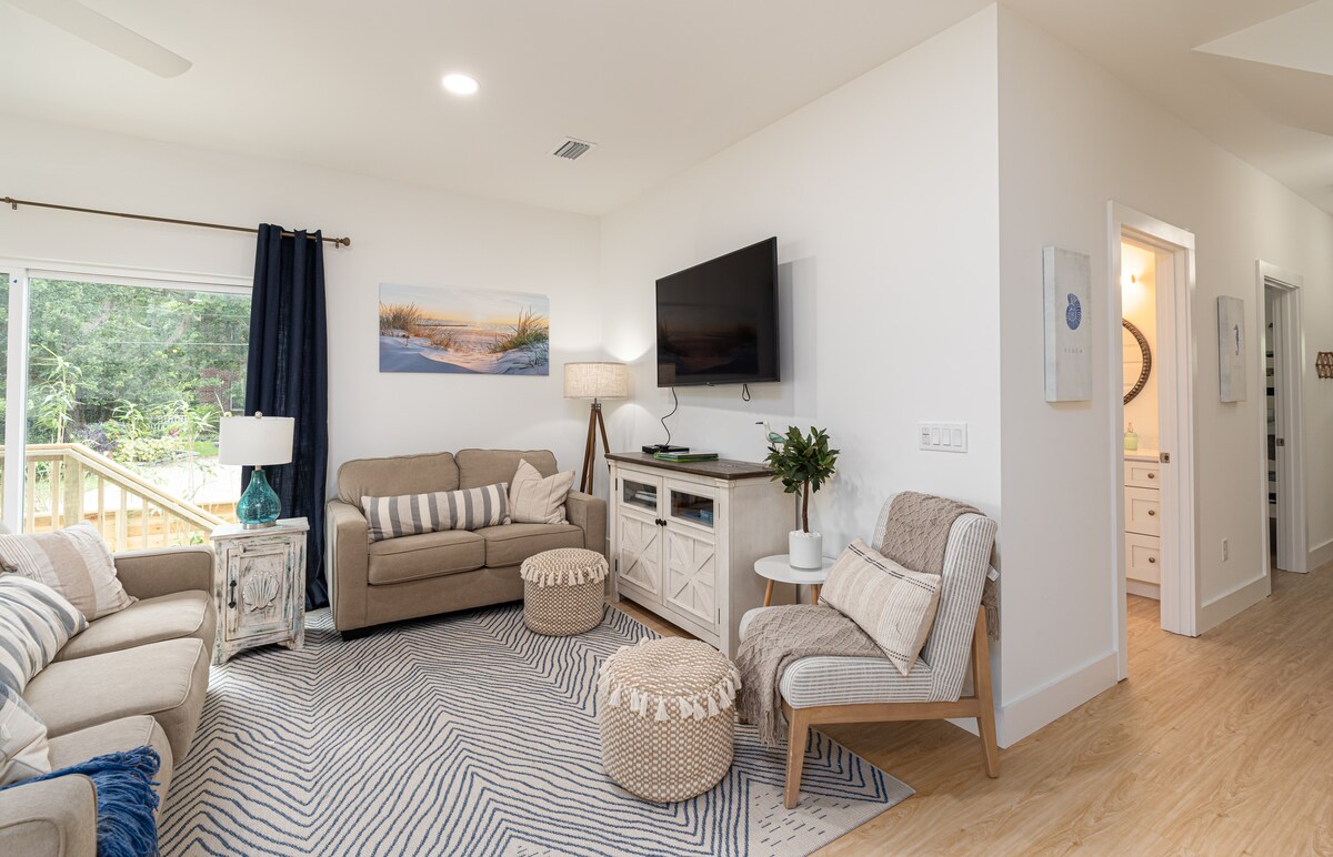 When the afternoon heat wins, everyone drifts in here. The TV goes on, the good armchair gets claimed early, and the guest bathroom is right around the corner for the sandy ones coming in from outside the house.
