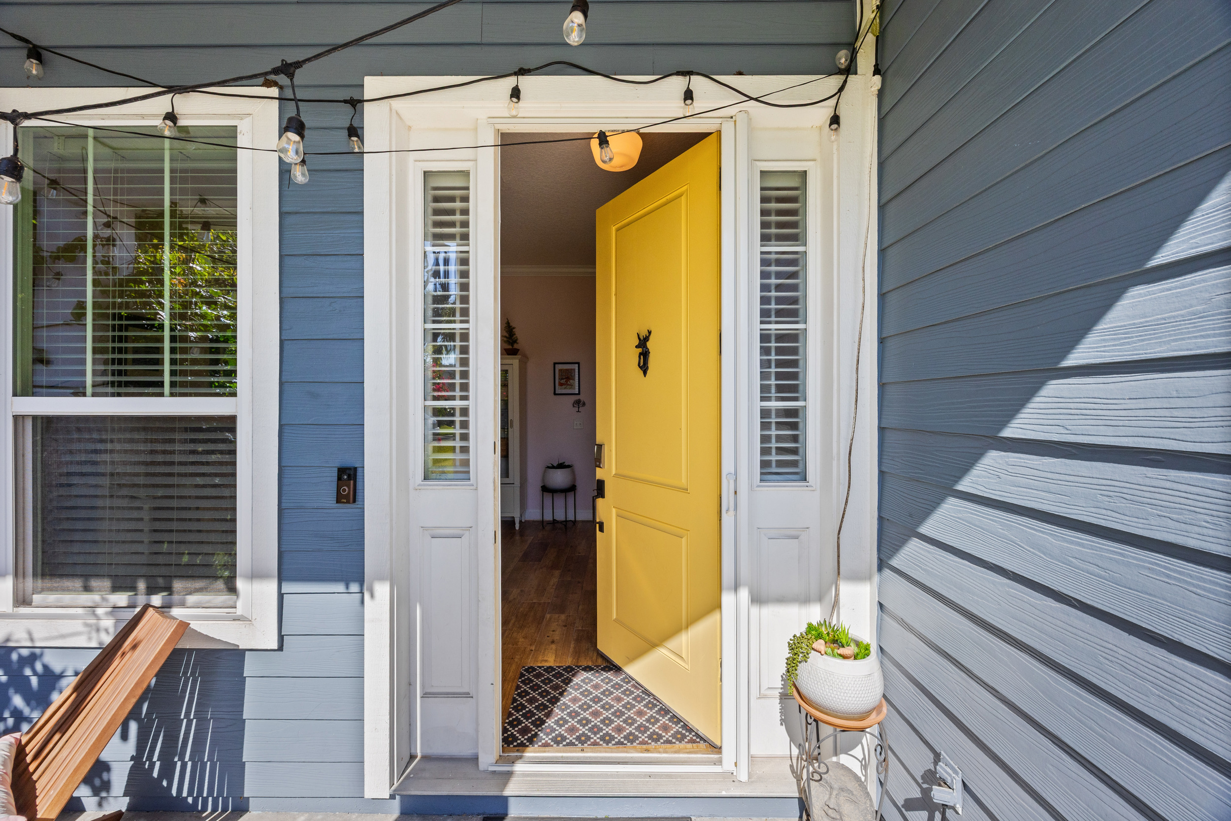 Cheerful Yellow Front Door Entrance
A vibrant yellow front door opens into a warm, inviting interior. Blue siding, white trim, and outdoor lighting create a welcoming first impression for guests.