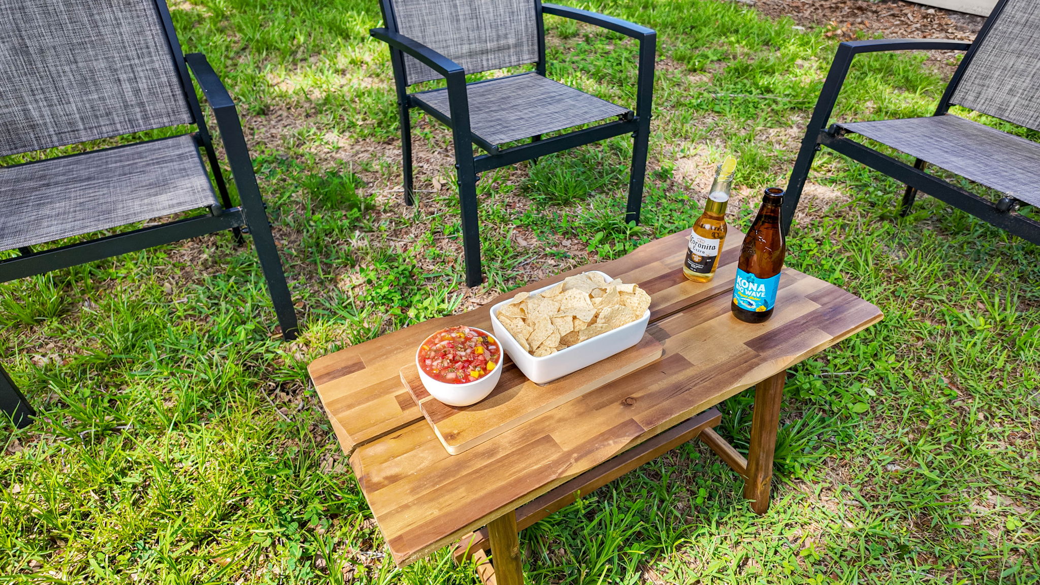 Four modern black patio chairs circle a small wood coffee table, styled with snacks, drinks, and a casual vibe.