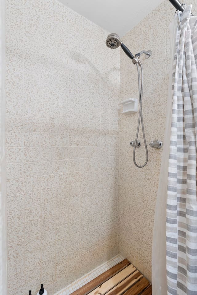 Walk-in shower with handheld sprayer and wood tile floor adds rustic charm to your daily routine.