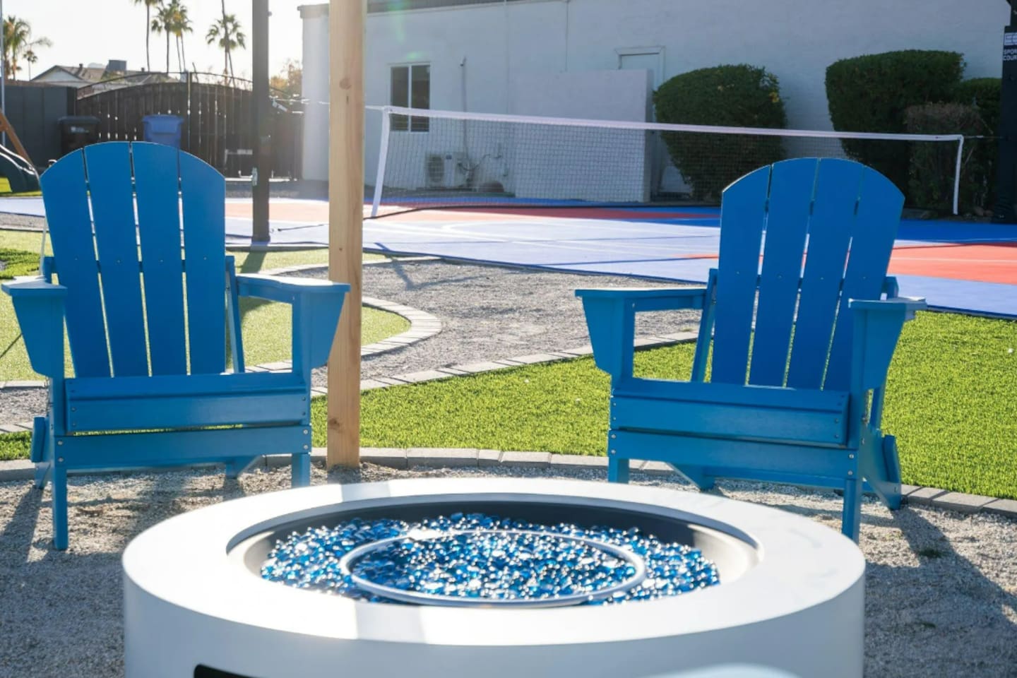 Blue Adirondack chairs circle the fire pit, with the sport court just steps away for guests who want to keep moving after dark.
