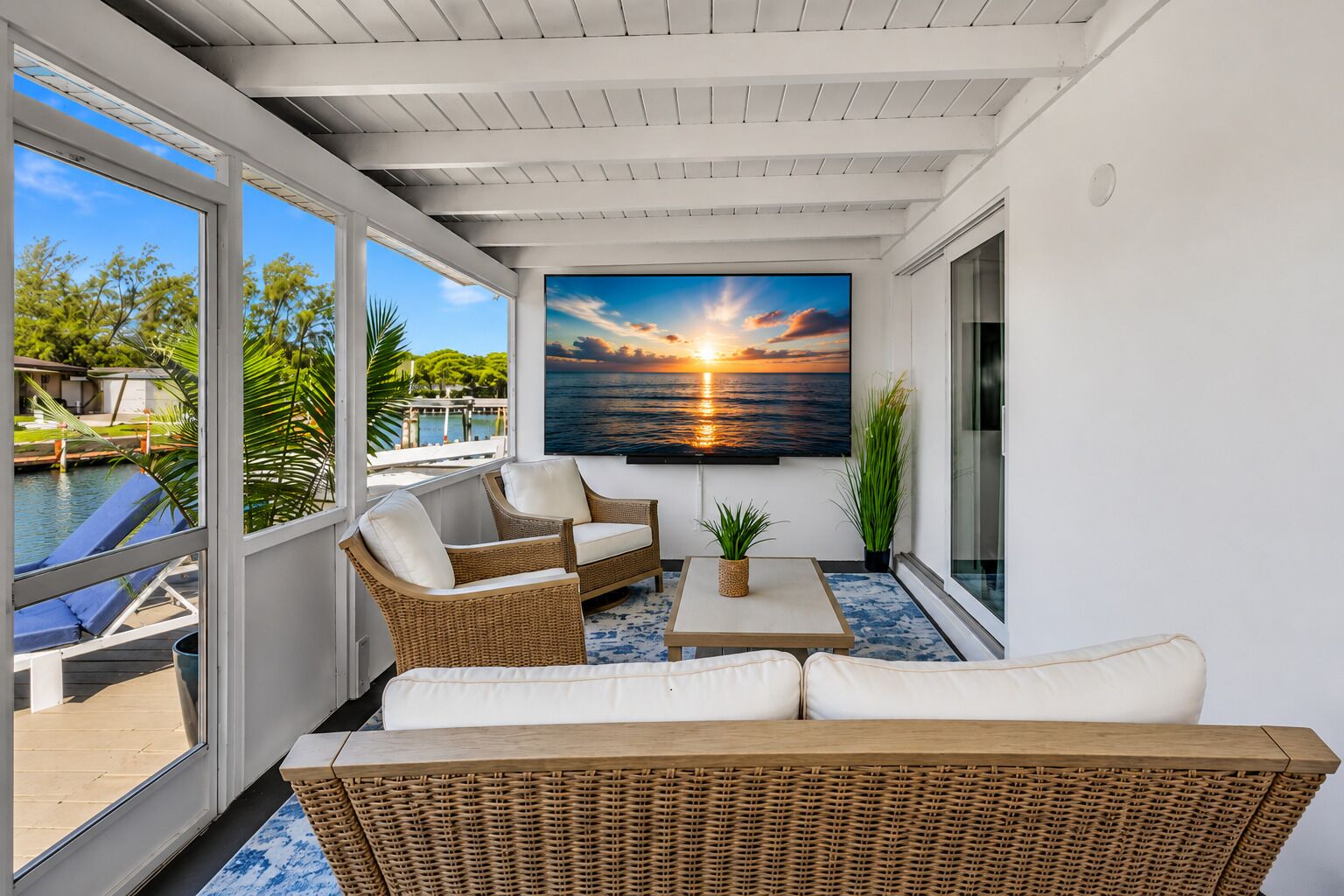 Screened waterfront patio with comfortable lounge seating, a 65” TV and canal views—perfect for relaxing after a day at the beach.