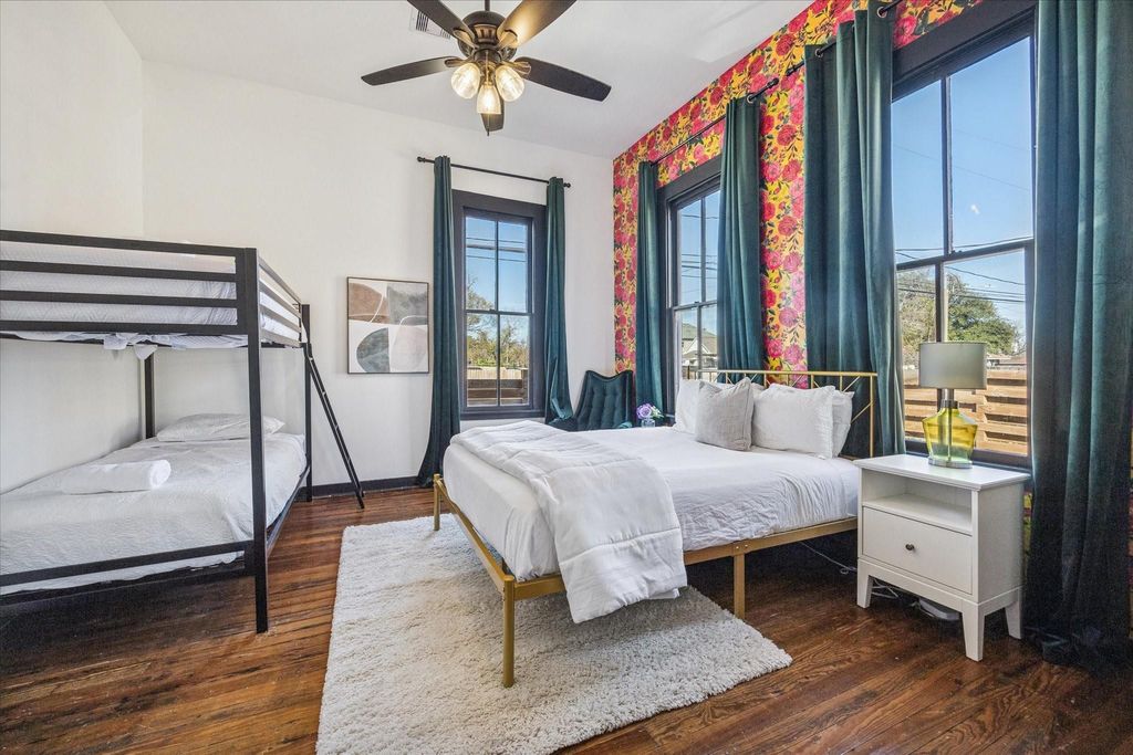 This inviting bedroom is filled with natural light and personality, featuring original hardwood floors, tall ceilings, and oversized windows framed by classic millwork. A nearby full bathroom and an additional bedroom just across the hall make this space e