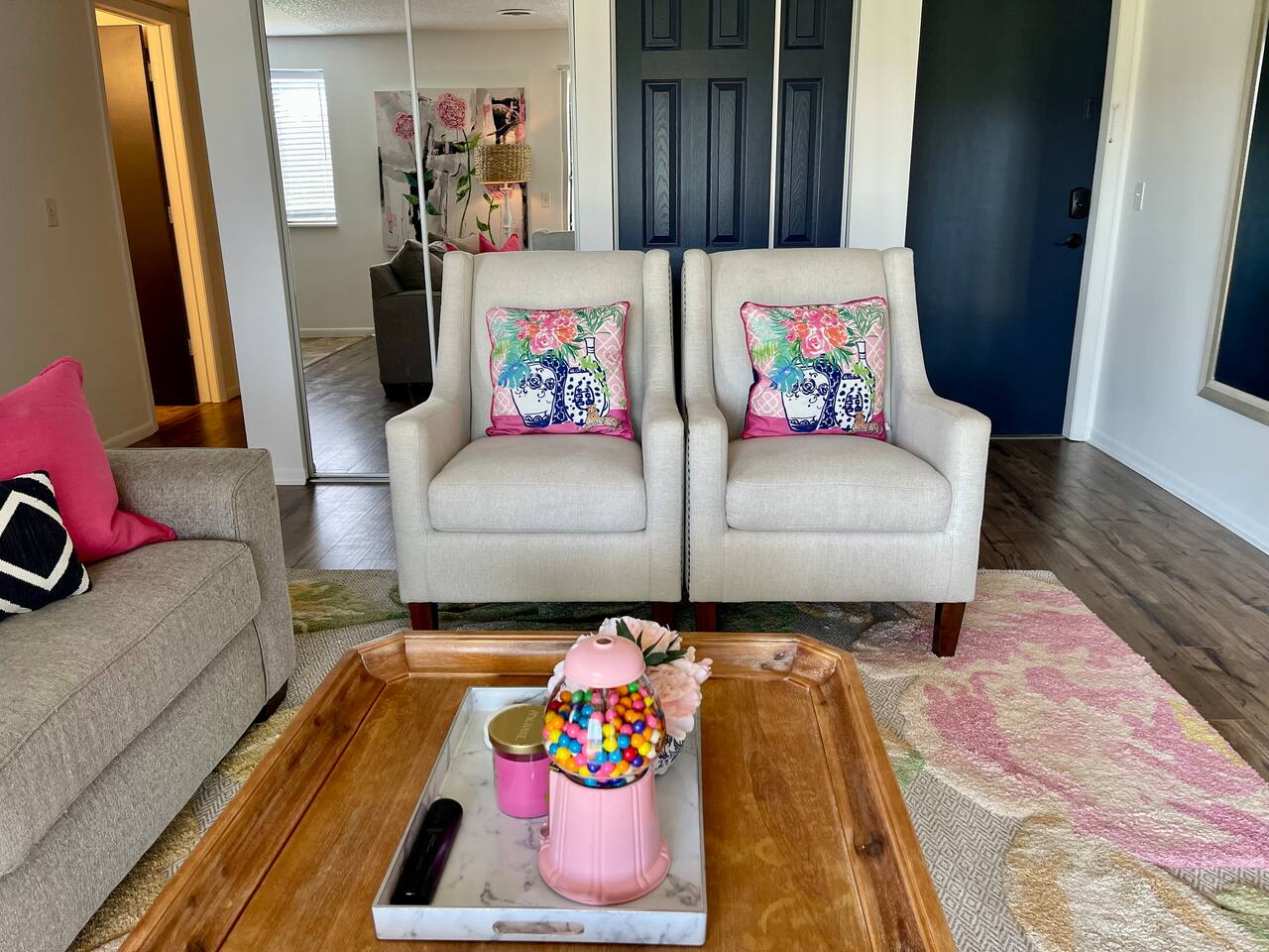 Bright and cheerful seating area featuring two comfy accent chairs with colorful floral pillows. A stylish wooden coffee table adds charm, topped with fun and welcoming decor—perfect for enjoying a cozy, relaxing stay with personality and warmth.