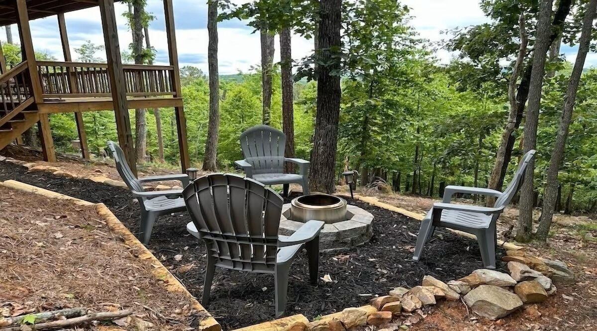 Private fire pit area beneath the trees, surrounded by Adirondack chairs - perfect for evening fires and mountain conversations.