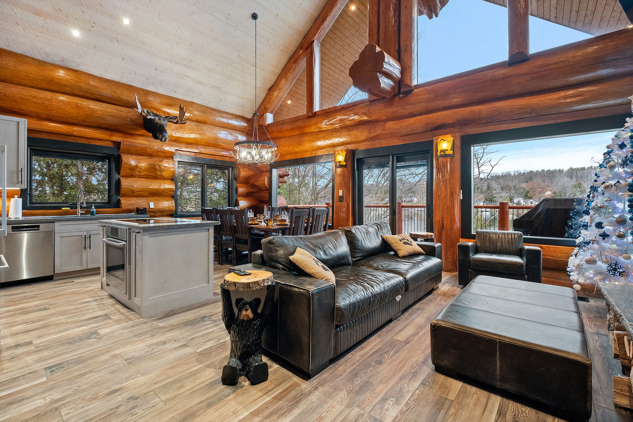 Bright and inviting main living area featuring a large sectional sofa, handcrafted log beams, and stunning views overlooking the lake.